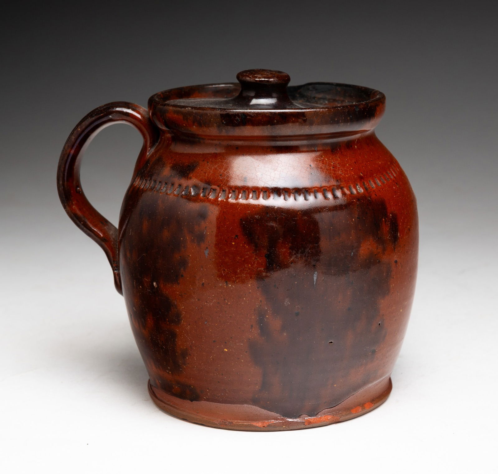 REDWARE HERB OR STEW POT.: REDWARE HERB OR STEW POT. American (Pennsylvania), 19th Century. One-handled jug with spout and lid in an orange glaze with mottled brown decoration, incised band at shoulder. 5.25"h. 5.75"w. From the