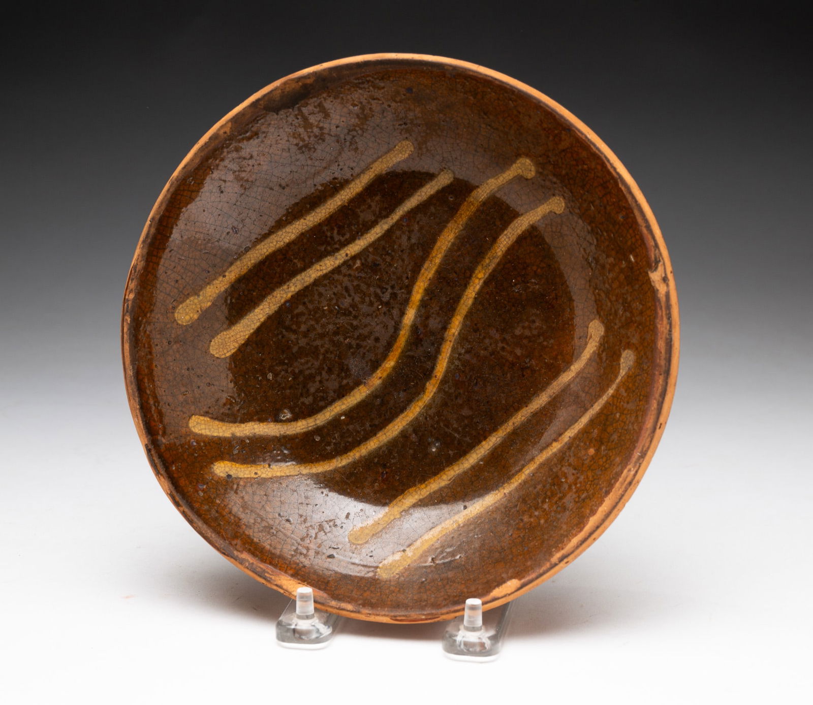 SLIP DECORATED REDWARE SHALLOW BOWL.: SLIP DECORATED REDWARE SHALLOW BOWL. American, 19th Century. Chocolate glaze decorated with six wavy yellow-slip lines. 1.5"h. 7.5"d. From the collection of Carol Schulman (Chesterland, Ohio).
