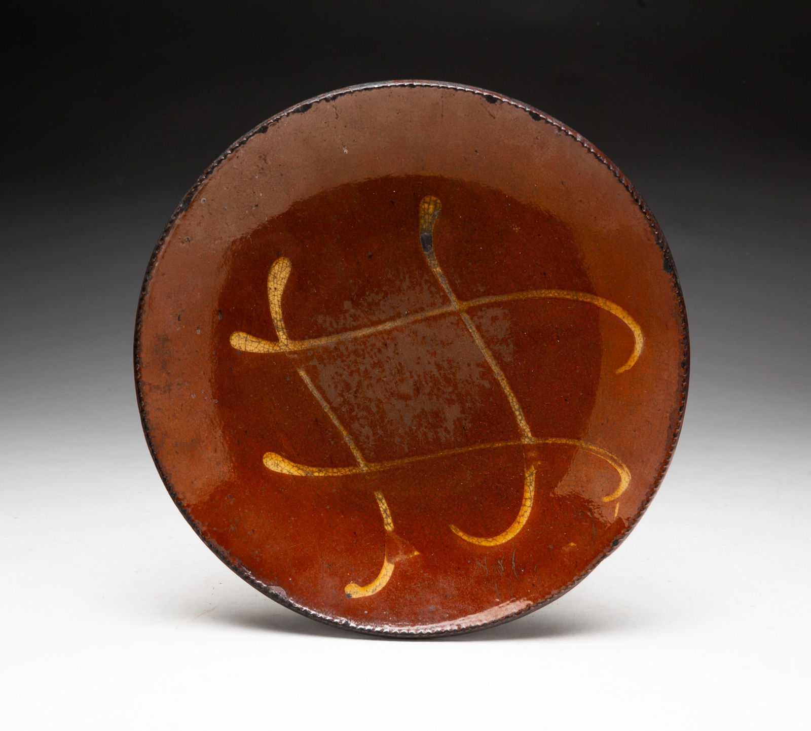 SLIP DECORATED REDWARE PLATE.: SLIP DECORATED REDWARE PLATE. American (Pennsylvania), 19th Century. Orange and black mottled glaze decorated with wavy perpendicular yellow lines, with coggled rim. 1.25"h. 9"d. From the collection o