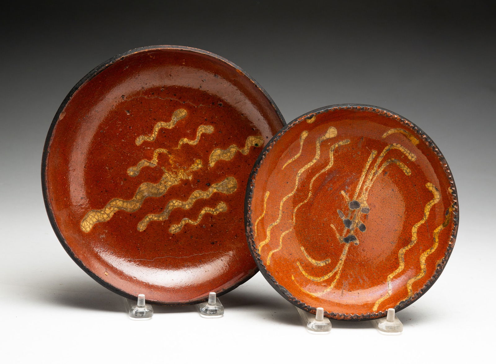 TWO SLIP DECORATED REDWARE PLATES.: TWO SLIP DECORATED REDWARE PLATES. American (Pennsylvania), 19th Century. Orange glaze decorated with five yellow squiggles,8.25"d. Orange mottled glaze decorated with yellow lines and squiggles, with
