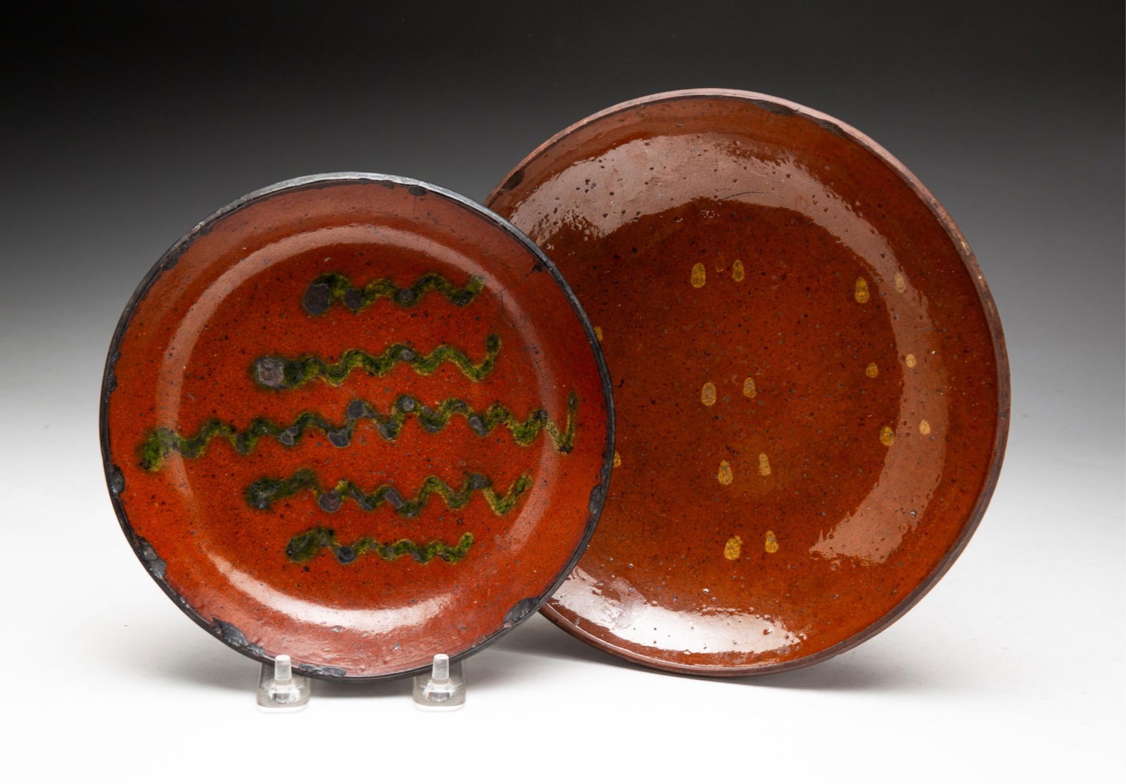 TWO SLIP DECORATED REDWARE PLATES.: TWO SLIP DECORATED REDWARE PLATES. American, 19th Century. Orange and black mottled glaze decorated with five green squiggly lines and black rim. 7.25"d. Orange and black mottled glaze decorated with