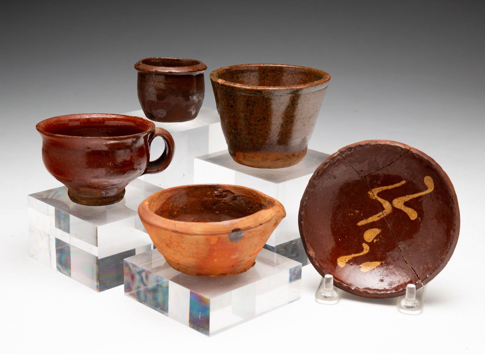 FIVE DIMINUTIVE PIECES OF GLAZED REDWARE.: FIVE DIMINUTIVE PIECES OF GLAZED REDWARE. American, 19th Century. Slip decorated plate with coggled rim. Repaired crack. 4"d. Handled teacup. 1.74"h. 3.5"w. Cup with no handle. 2.5"h. 3.25"d. Batter j