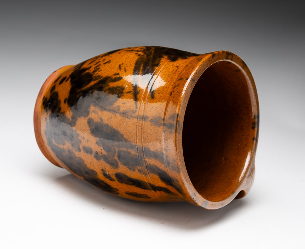 OVOID HANDLED REDWARE VESSEL.: OVOID HANDLED REDWARE VESSEL. American, 19th Century. Nicely shaped with applied handle, tan glaze with manganese mottling. 6.25"h.