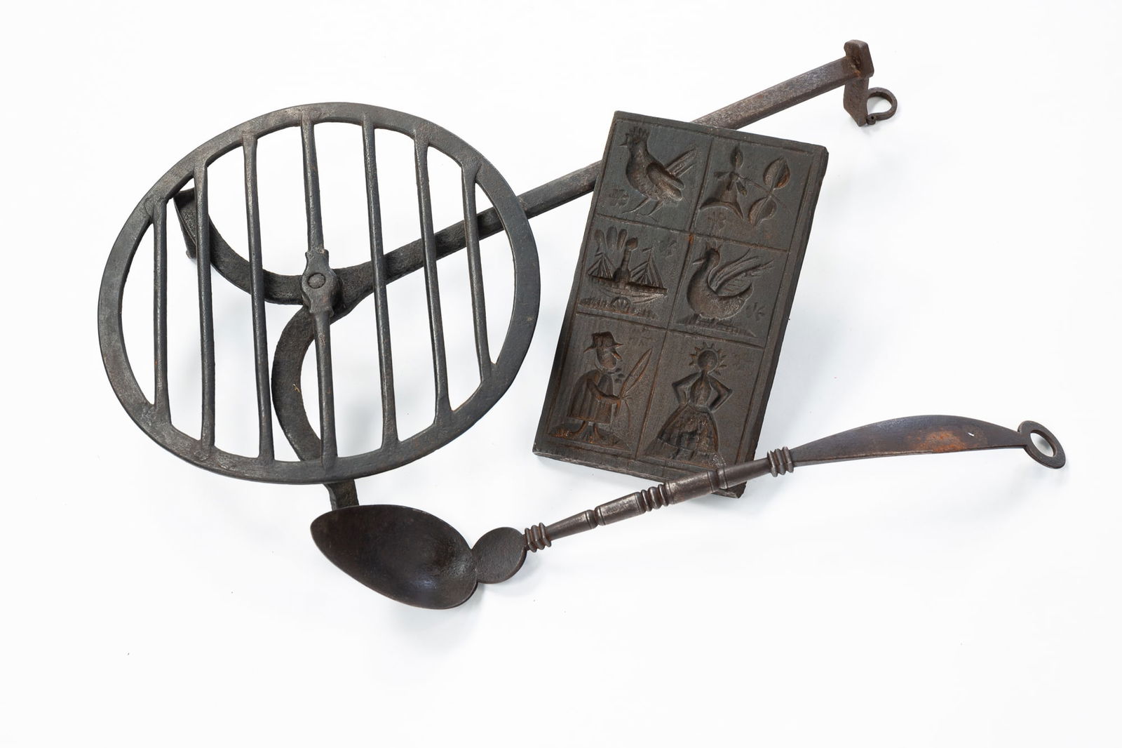 CAST IRON SPRINGERLE MOLD, TRIVET, AND SPOON.: American, 19th Century. Pictorial springerle mold depicting a ship, rooster, and husband and wife; an elegant Georgian iron spoon, and a tripod skillet. Trivet, 16"l.