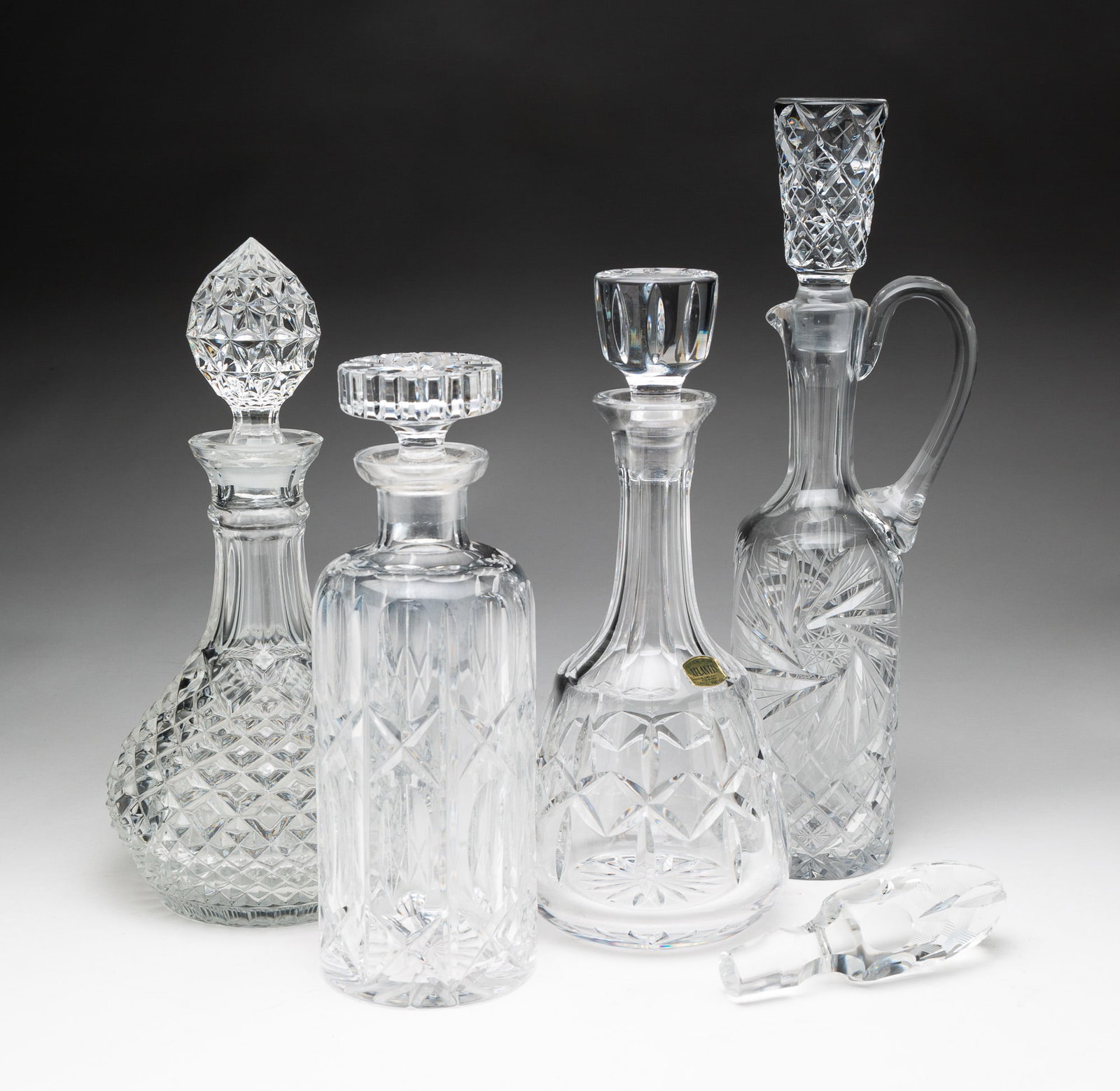 FOUR DECANTERS, ONE MARKED ATLANTIS.: American/Portuguese, 20th Century. Atlantis cut crystal decanter of tapered form; cut crystal decanter of round form; cut crystal decanter with handle and spout; and pressed glass decanter of bulbous 