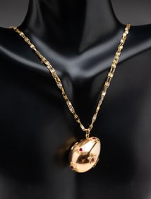 14K YELLOW GOLD NECKLACE WITH RUBY ACCENTED EGG LOCKET.