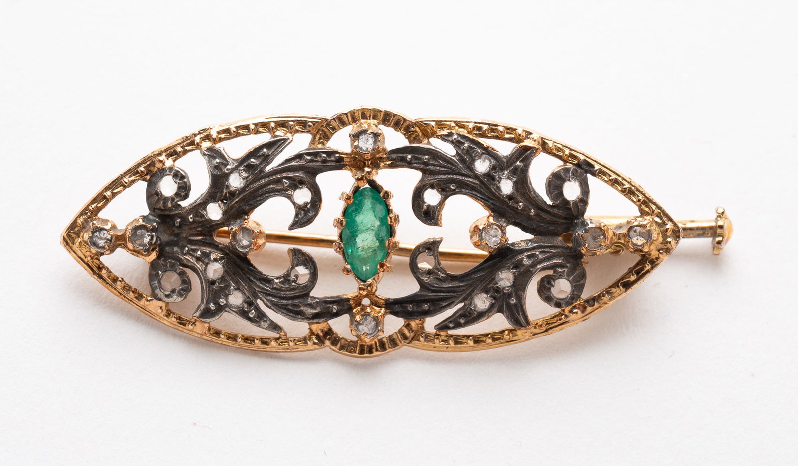 GOLD AND SILVER DIAMOND AND EMERALD BROOCH.: Circa 1900. 9k gold and silver. Openwork oval accented with twenty-four diamond and a center marquise emerald. Bayonet clasp. Approximately 2.95 dwt. **Note: Bidders who are not yet established with o