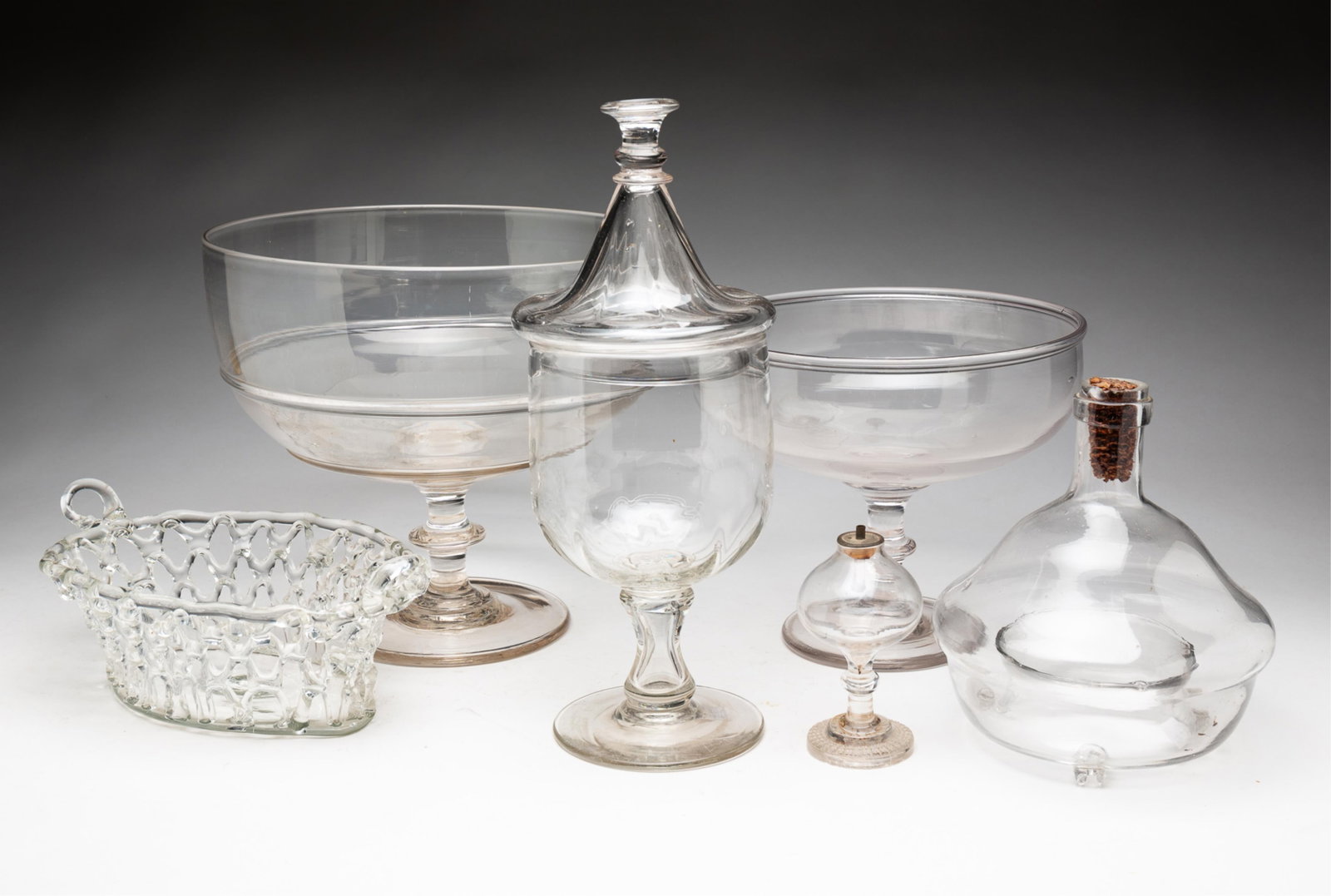 SELECTION OF EARLY BLOWN FLINT GLASS.: American, 19th Century. Two open compotes with knob stems and broken pontils. One with two rings around bowl, 9.25"h. 10.25"I. And the second with folded rim, 4.5"h. 8.75"d. A sparking lamp, knob stem