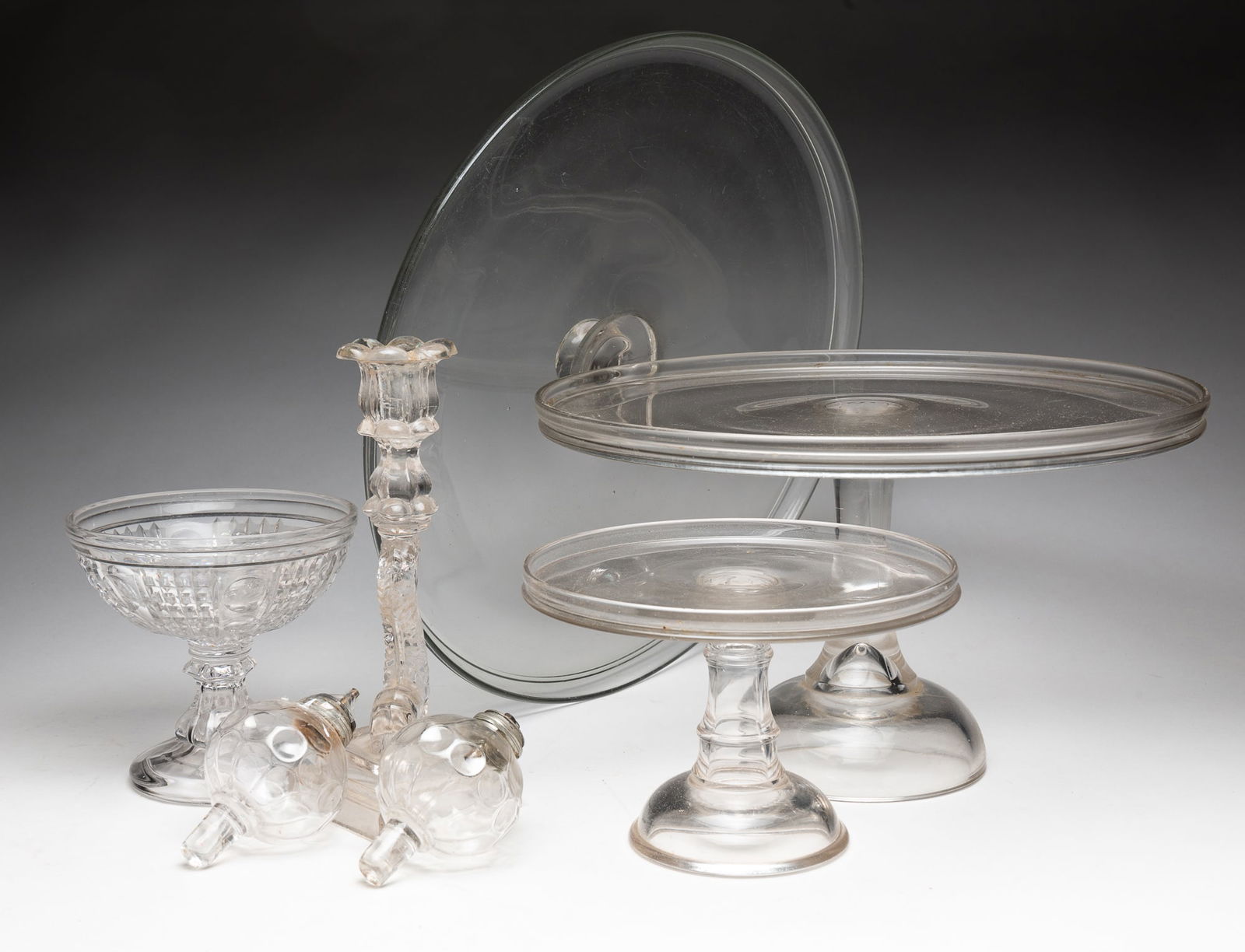 COLLECTION OF CLEAR GLASS ITEMS INCLUDING WHALE OIL PEG LAMPS AND CAKE STANDS.: American, 19th/20th Century. Two blown molded whale oil peg lamps with pewter collars, two pressed glass pedestal cake stands, a cut crystal pedestal compote, a glass candlestick in a koi fish motif,