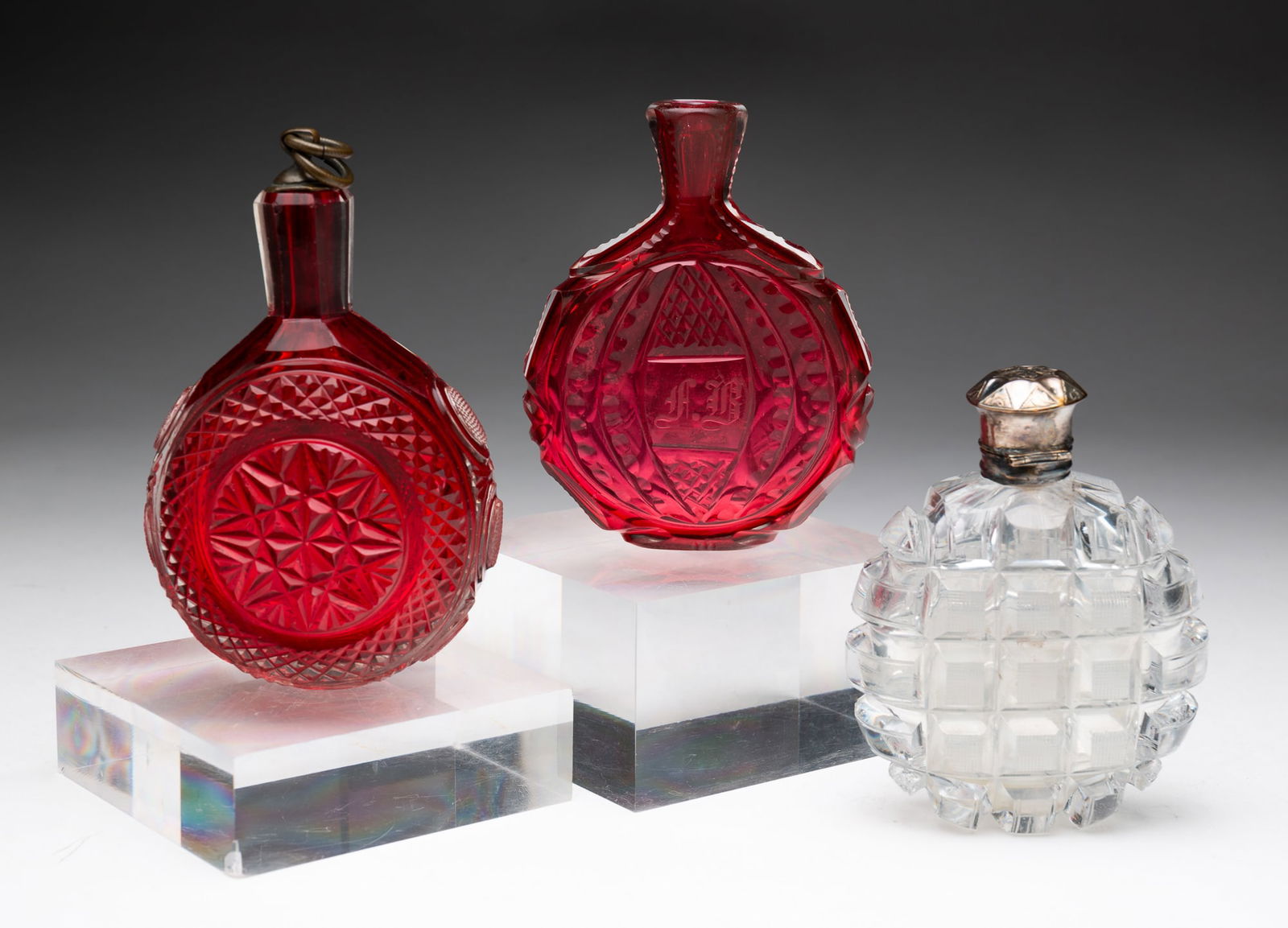 THREE BLOWN AND CUT GLASS FLASKS.: European, 19th Century. Two are cranberry cased in clear, the flatter of the two is initialed "F.R.", 4"h., and the third is clear with interior stopper and silver plated hinged lid, 3.75"h.