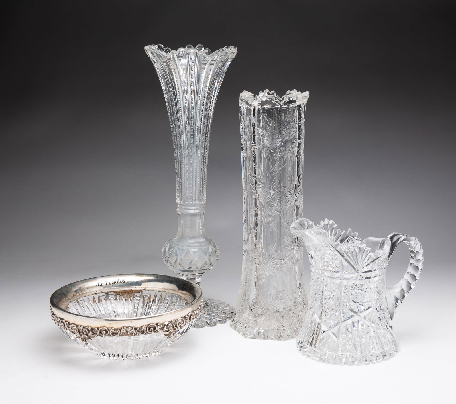 FOUR PIECES OF BRILLIANT PERIOD CUT GLASS.: American, circa 1900. A bowl with starburst bottom, ribbed and notched sides and sterling silver rim floral and foliate castings by J.F. Fradley, chips, 2.5"h. 7"d. A juice pitcher with starburst, not
