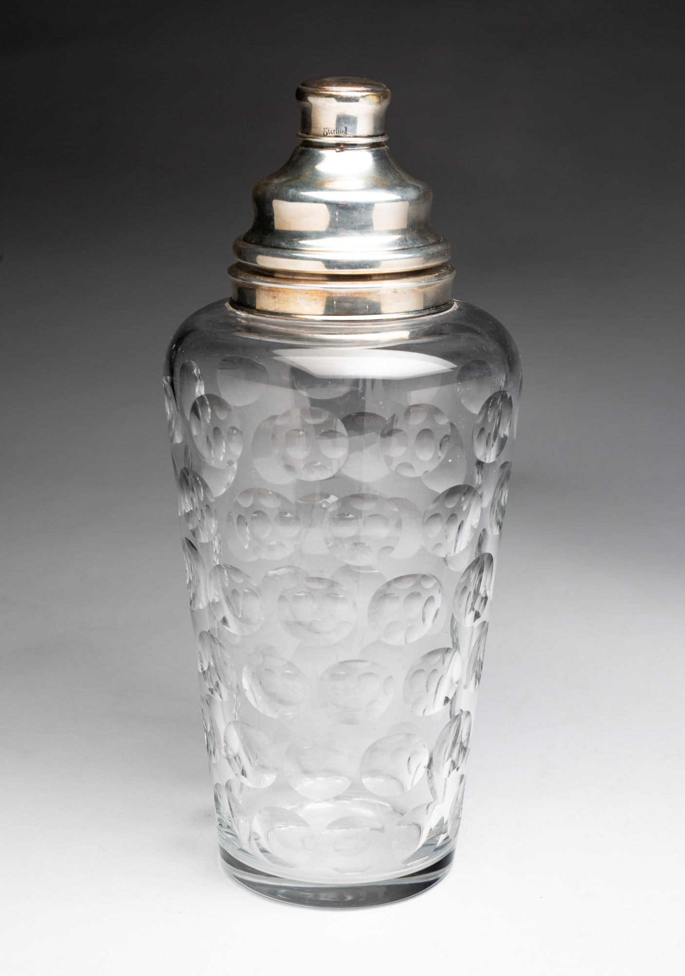 CUT GLASS COCKTAIL SHAKER WITH STERLING MOUNTS.: American, 20th Century. Canted sides, rounded shoulders and cut "thumbprint" pattern. Sterling collar, strainer and cap. 12"h.