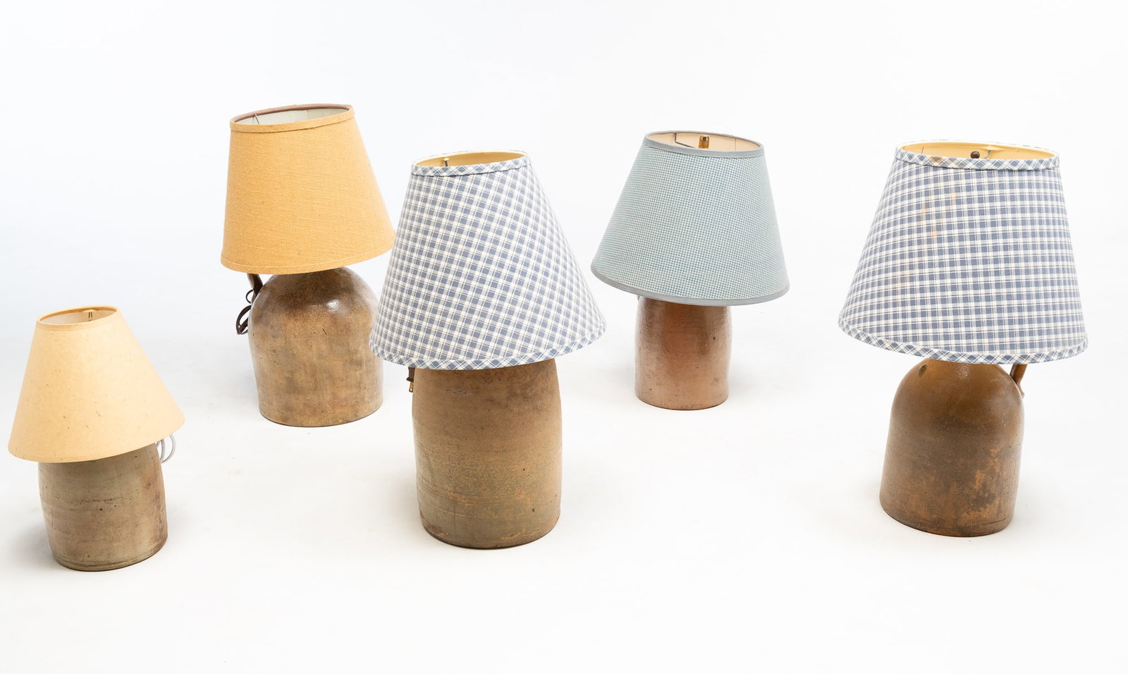 FIVE ELECTRIFIED STONEWARE JUG LAMPS.: American, 19th/20th Century. With applied handles, cords with plugs, harps with finials, and shades. Tan and brown salt glazed jug stamped "P. Olivier Grocer & Wine Merchant Corner King & Wellington S
