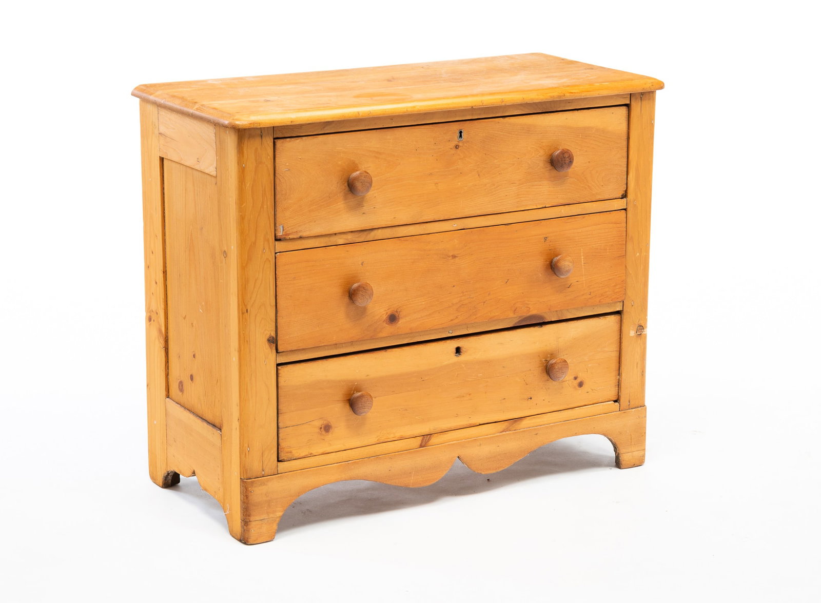 COUNTRY THREE DRAWER CHEST.: American, 19th Century. Pine. Simple construction with square cut nails, having a single board top over three drawers with wood knobs, paneled ends, having a shaped apron and cut out feet. 29.75"h. 35