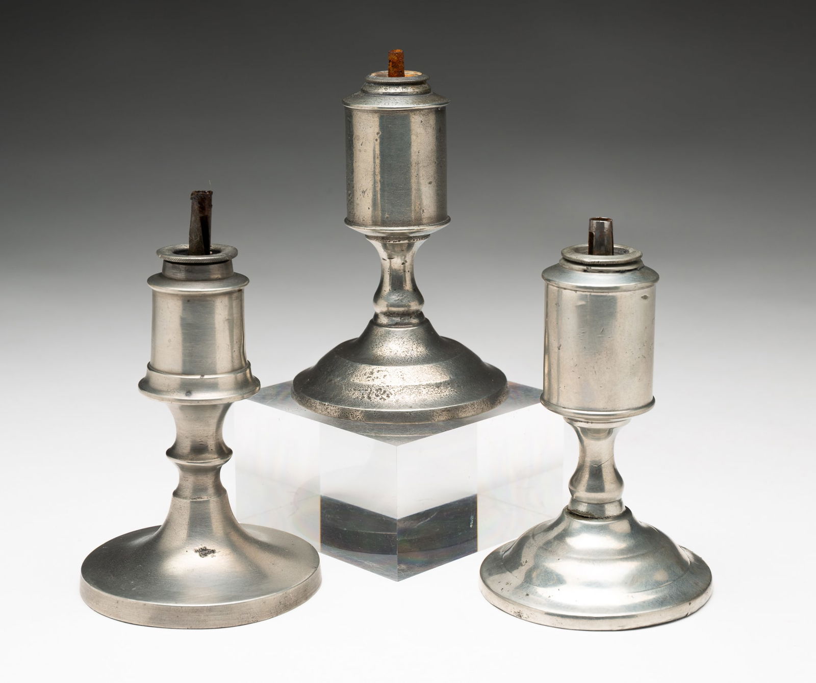 THREE PEWTER WHALE OIL SPARKING LAMPS.: American, 19th Century. A pair marked Dunham, single burners, can shaped fonts and baluster stems, 4.5"h. And one is unmarked, single burner, font with canted sides and knob stem, 5"h.From the Collect