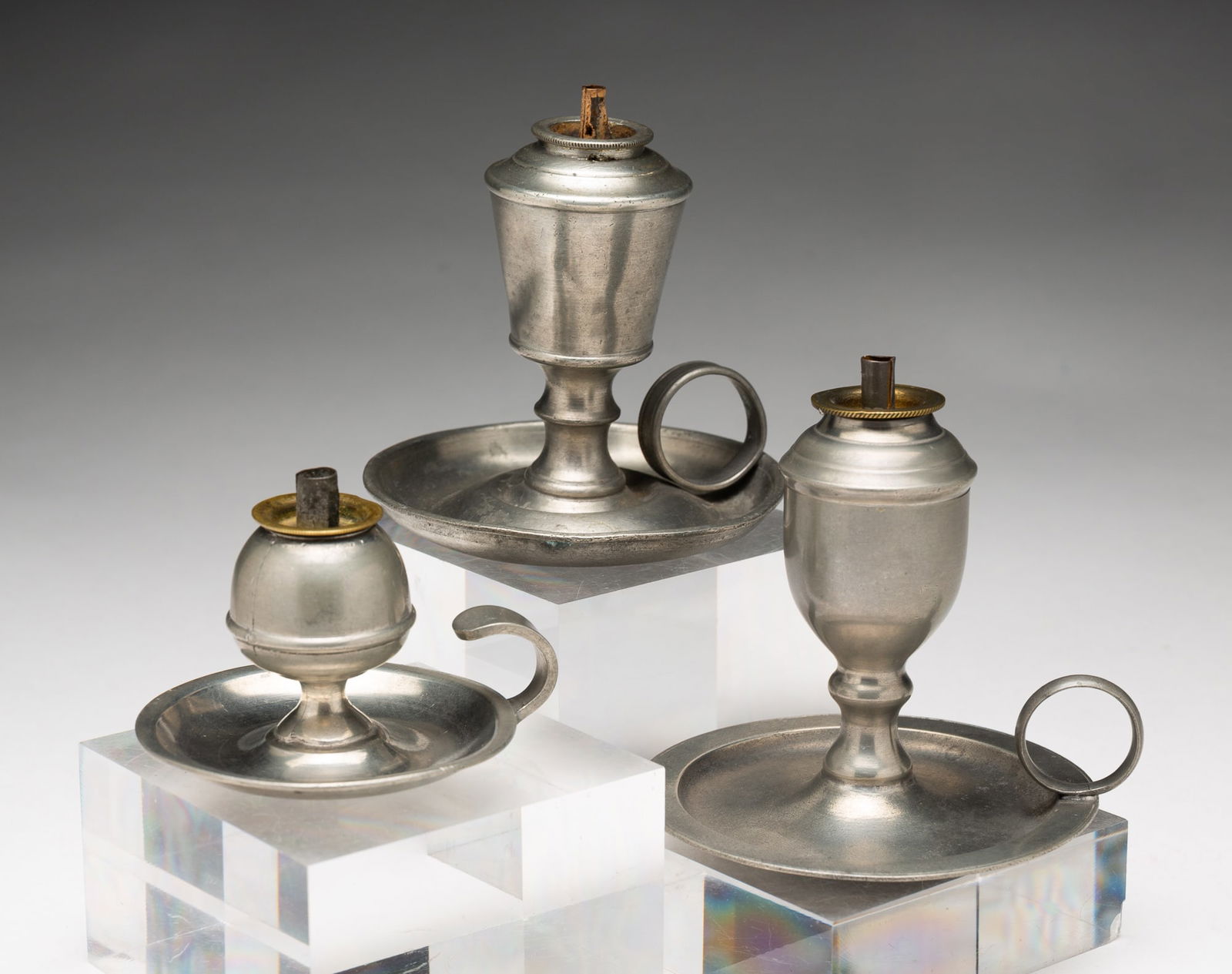 THREE PEWTER WHALE OIL SPARKING LAMPS.: American, 19th Century. All three have single burners and handled saucer bases. One marked Putnam with saucer base having flat edge, 3.75"h. The second marked Calder with can font with canted sides, 3