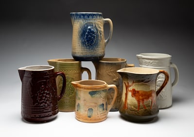 SEVEN MOLDED AND GLAZED STONEWARE PITCHERS.
