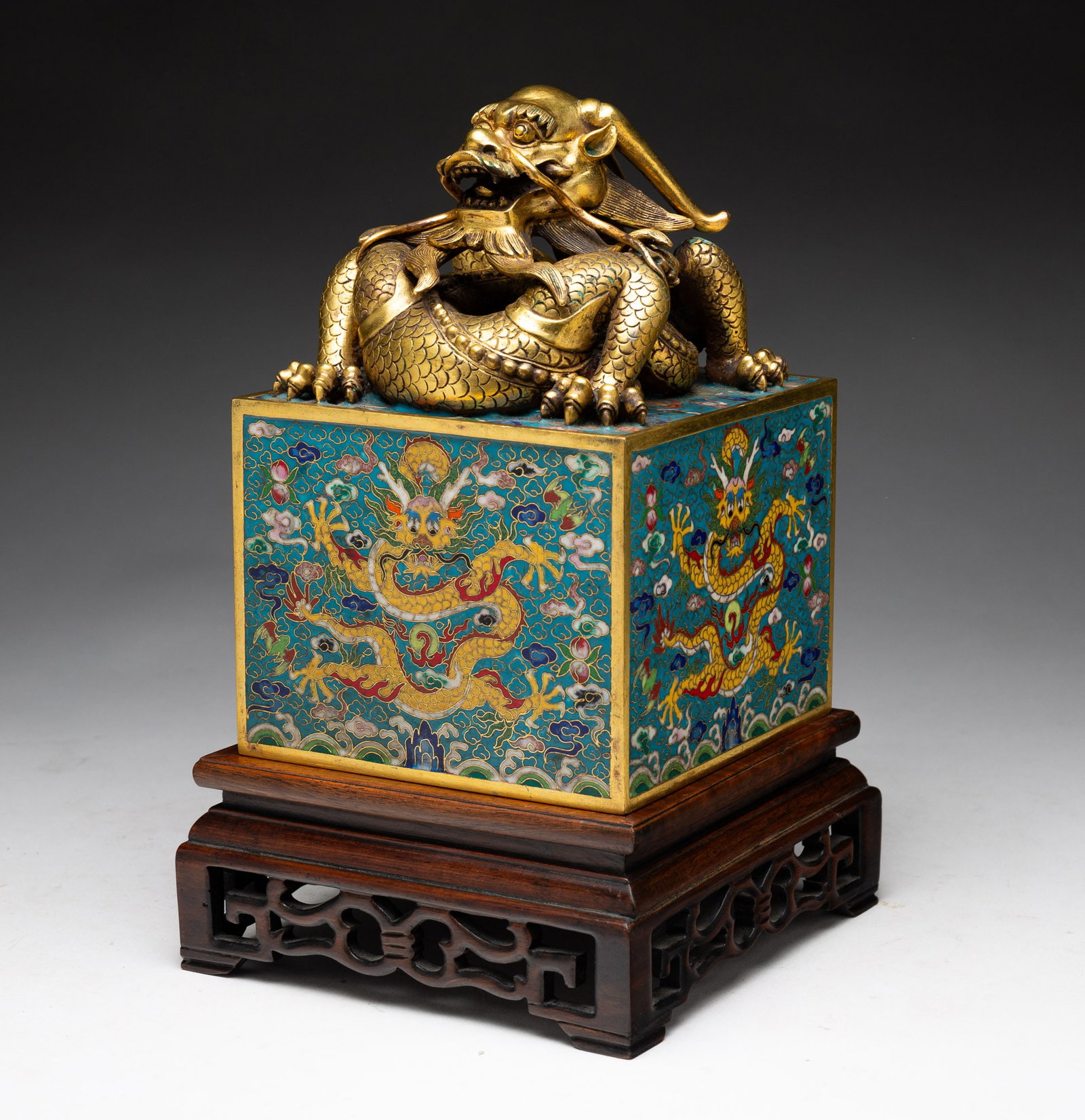 CHINESE IMPERIAL GILT BRONZE AND CLOISONNE DRAGON SEAL.: China, 19th or 20th Century. Having a gilt bronze four-clawed dragon coiled atop a cloisonne cube, each side depicting a yellow five-footed and five-clawed dragon amid swirling clouds and double peach