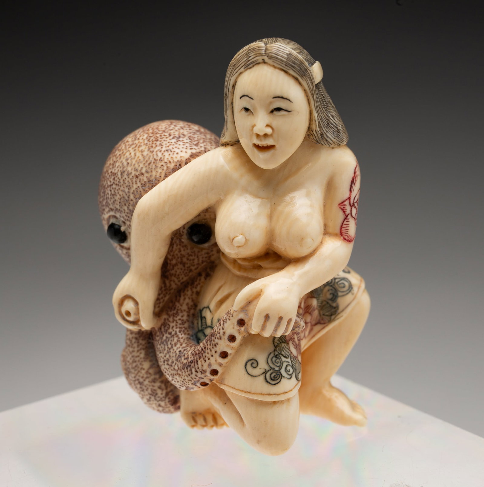 JAPANESE CARVED SHUNGA NETSUKE.: Japan, circa 1900. Carved, incised, and colored natural material. Depicting a woman and an octopus in an erotic embrace, signed. 2"h. 2"w.
