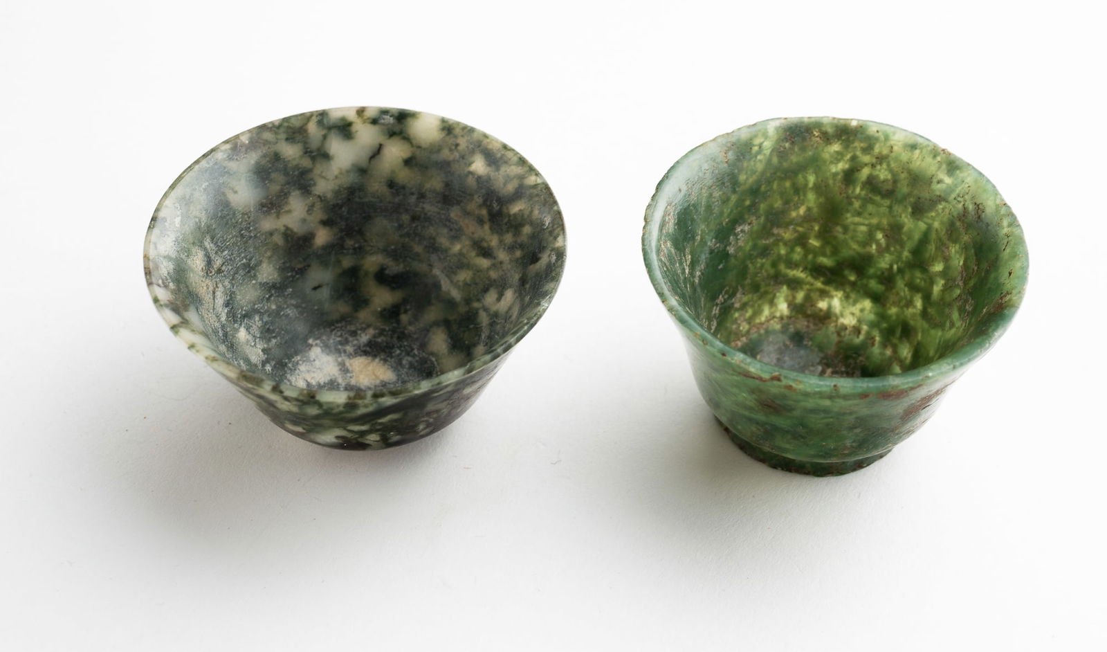 TWO VINTAGE CARVED SPINACH JADE WINE CUPS.: Chinese. Two cups - each measuring approx. 1.12"h. One measuring 1.62" across the top, one measuring 1.87" across top.