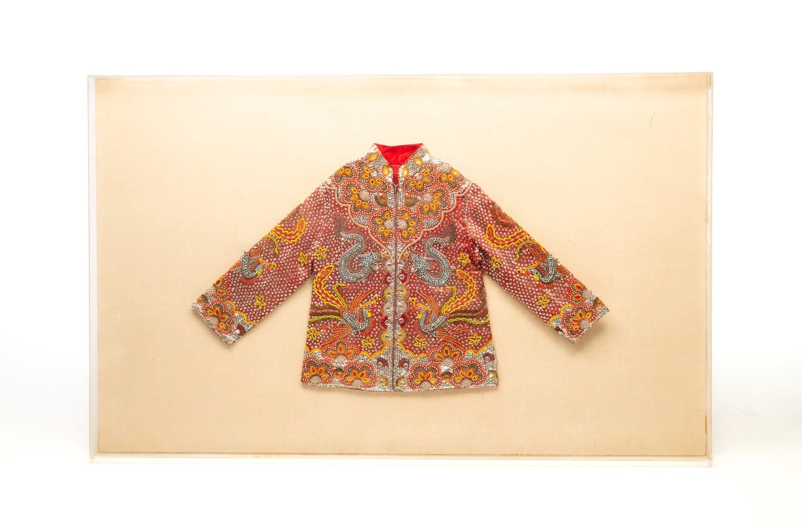 MOUNTED BEJEWELED BLAZER.: 20th Century. Heavily bejeweled zip up blazer in red. Mandarin collar blazer with dragon, phoenix, and flower motif. In plexiglass case. 37"h. 60.5"w.