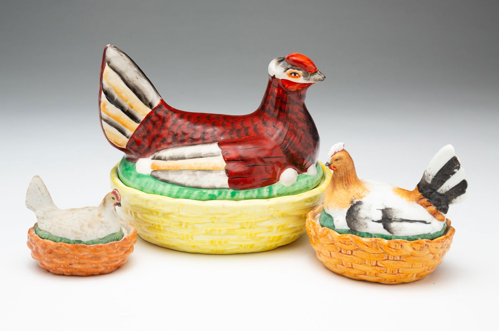 THREE STAFFORDSHIRE HENS ON NESTS.: England, 19th Century. The largest has multicolored high glaze. 4.5"h. 5''w., middle size and smallest with matte glazes. 3''h. 3.25''w. and 2"h. 2.5"w.