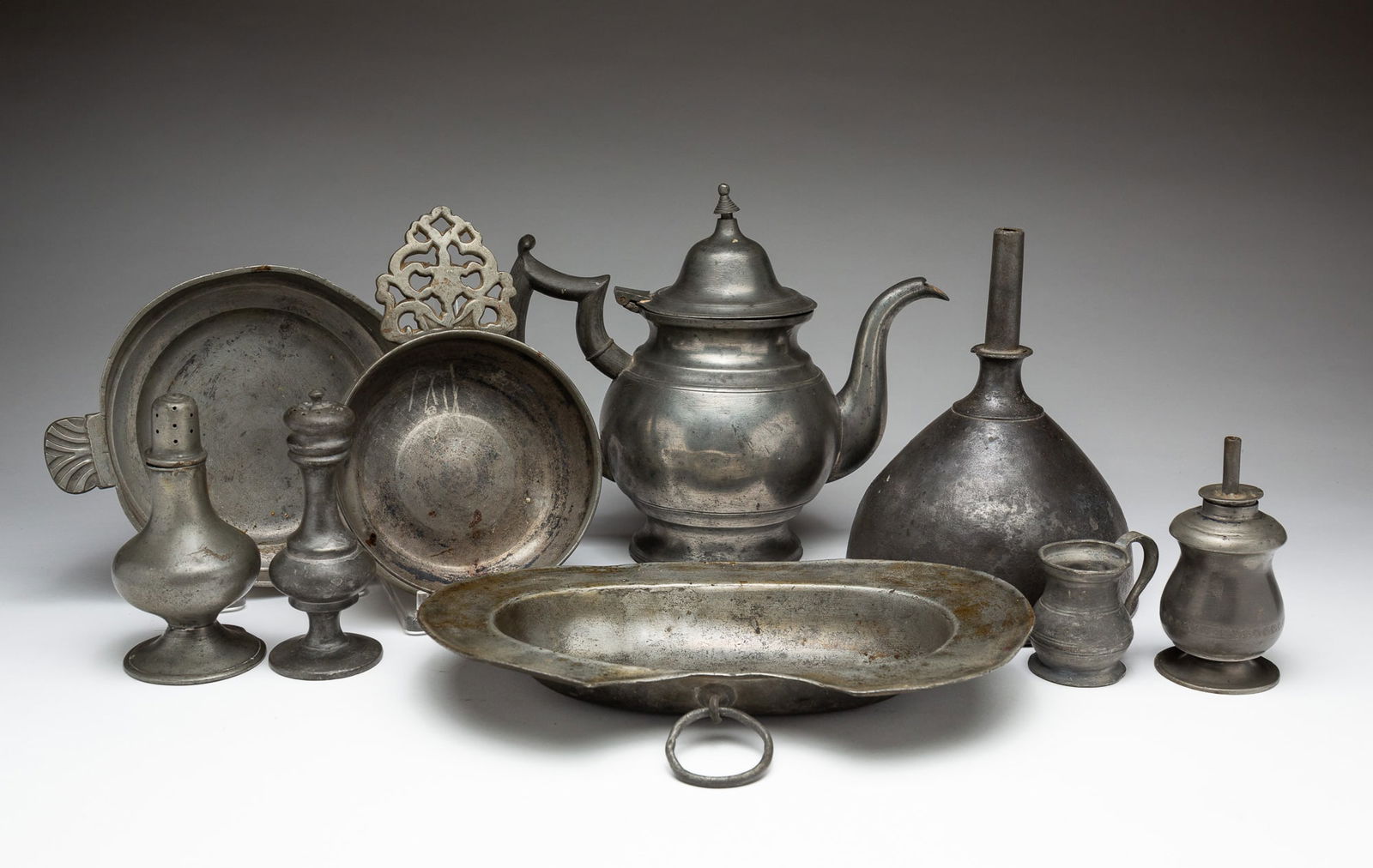 COLLECTION OF PEWTER.: European and American, 19th Century. A teapot marked T.D. &.S.R., 7.5''h., wine funnel, 7"h. Ashaving dish with hallmarks, 10"w. 6"d. Two pepper pots, 5"h and 4.5''h. Porringer with open handle, 7.25"