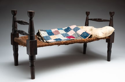 WOODEN DOLL BED WITH A PIECED DOLL QUILT AND A PILLOW.