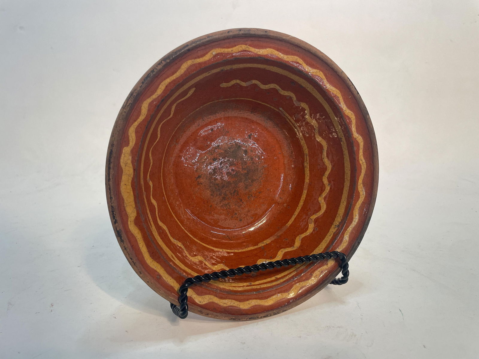 SLIP DECORATED REDWARE BOWL.: American (Pennsylvania), 19th Century. Having a flared rim and orange and black mottled glaze, the center decorated with bands of straight wavy lines in yellow slip. 3"h. 8.5"d. From The Lifetime Coll
