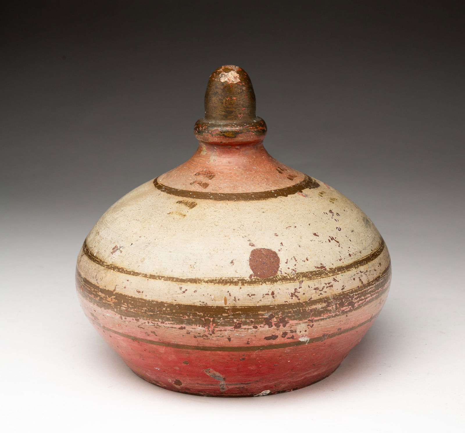 AMERICAN PAINTED RED CLAY DOORSTOP.: American (Ohio), ca.1900. Bulbous round shape with acorn finial, white and red paint with gold acorn and horizontal stripes. 6"h. 6.25"d.