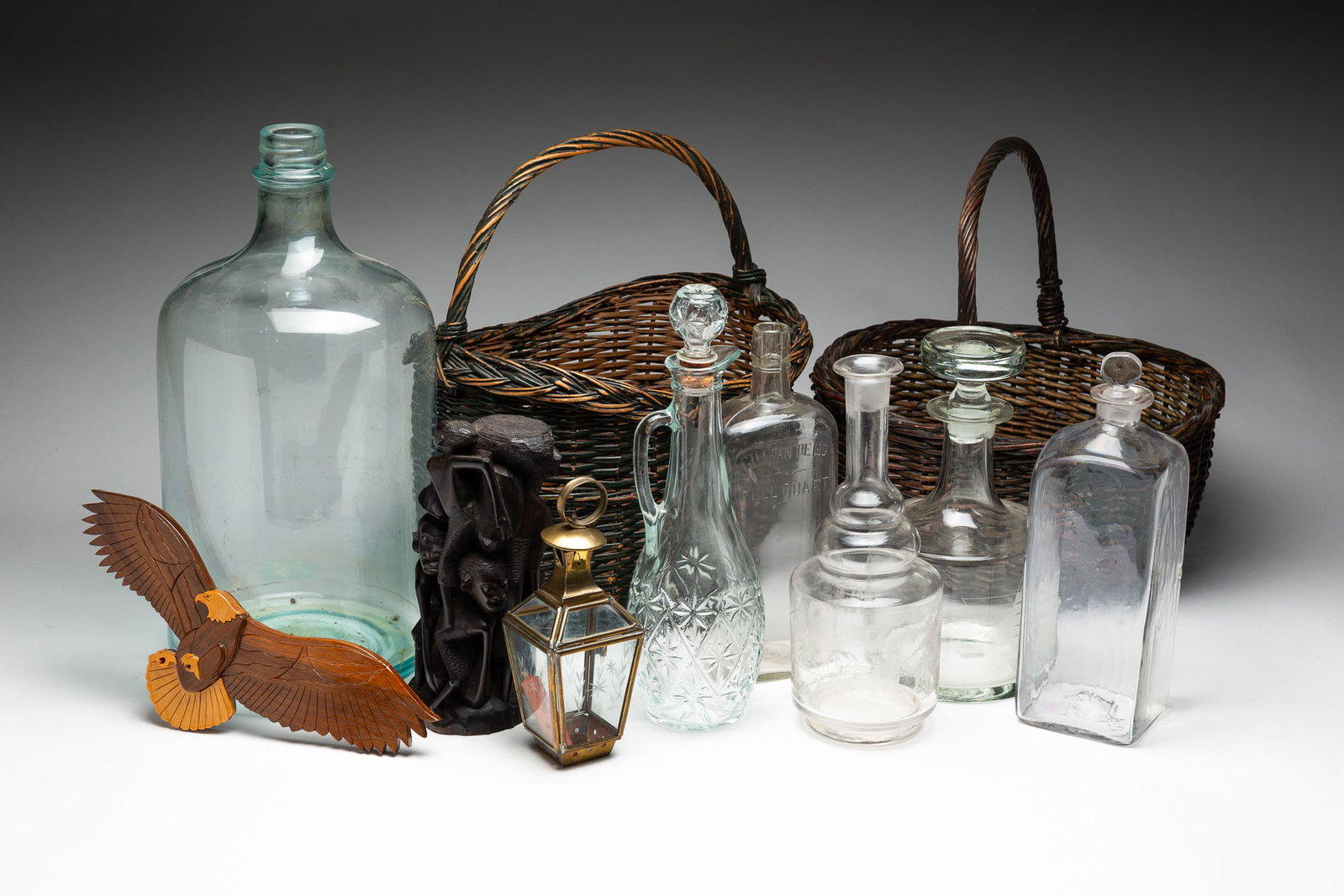 ECLECTIC GROUP OF DECORATIVE ARTS.: International, 20th Century. Comprising a square form glass decanter, a round glass decanter etched with a ship, a pressed glass decanter, a round decanter etched with Asian motifs, a glass quart bott