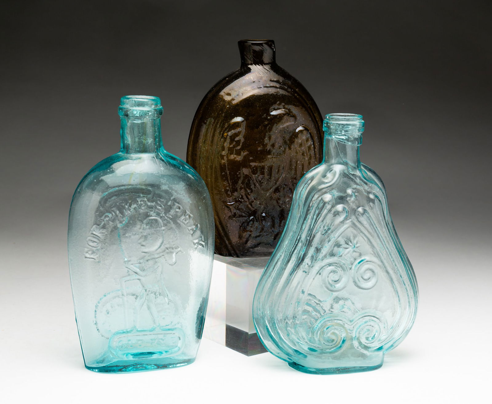 THREE AMERICAN MOLD-BLOWN GLASS FLASKS, INCL. PIKE'S PEAK OLD RYE.: American, 19th Century. "For Pike's Peak, Old Rye" with hiker on one side and eagle over an oval reserve and "Pittsburgh, Pa" on reverse. 7.75''h. An amber cornucopia and eagle flask with broken ponti