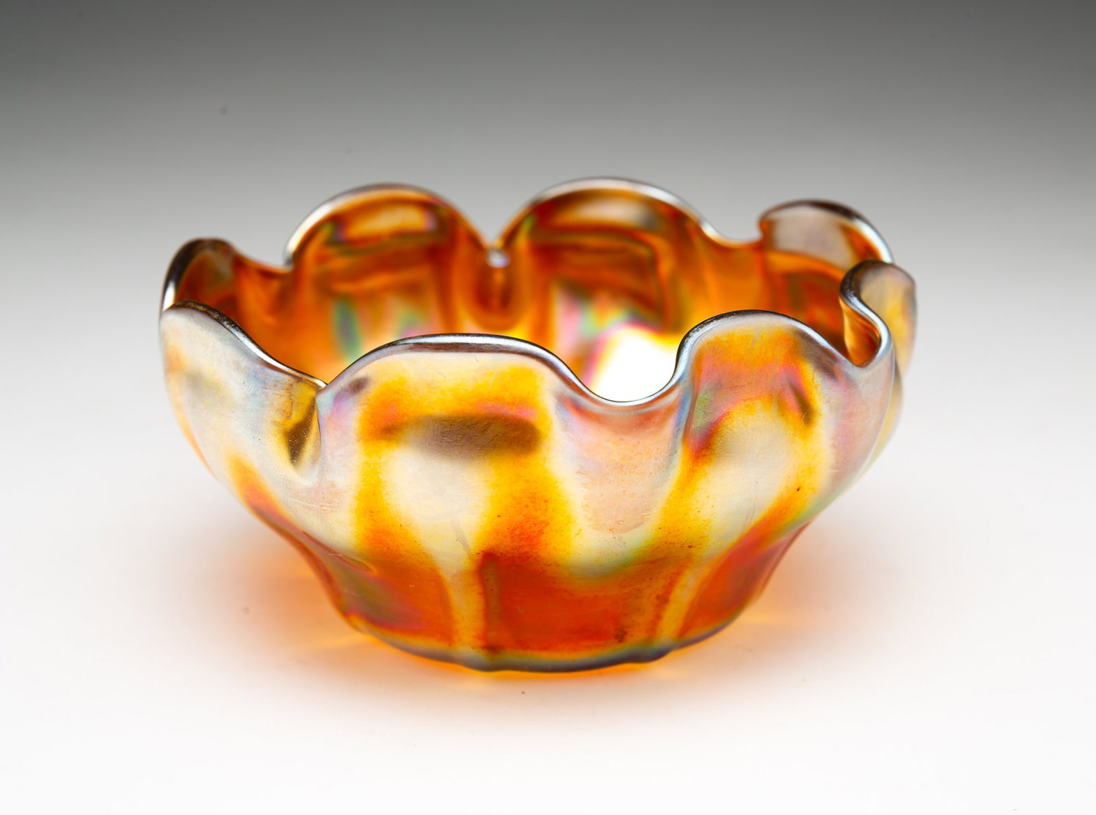 TIFFANY FAVRILE FINGER BOWL.: American, Early 20th Century. Amber glass iridizing with crimped scalloped rim. Signed "L.C.T." to bottom. 2.25"h. 4.5"d.