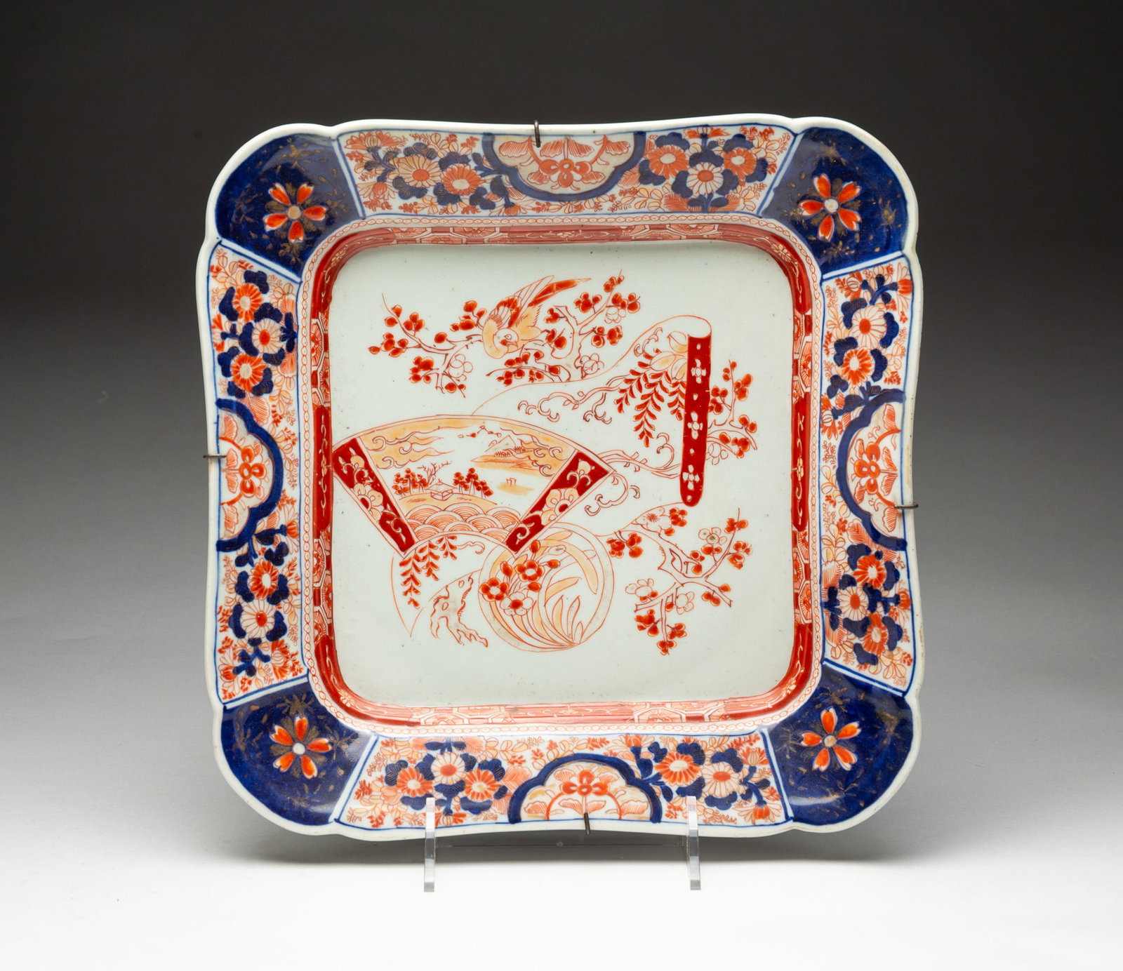 IMARI SQUARE SHALLOW BOWL.: China, 19th Century. Porcelain. Shaped rim, rounded corners, floral pattern with scenic fan at center in rusts, tans and cobalt blue glazes. 13" square.