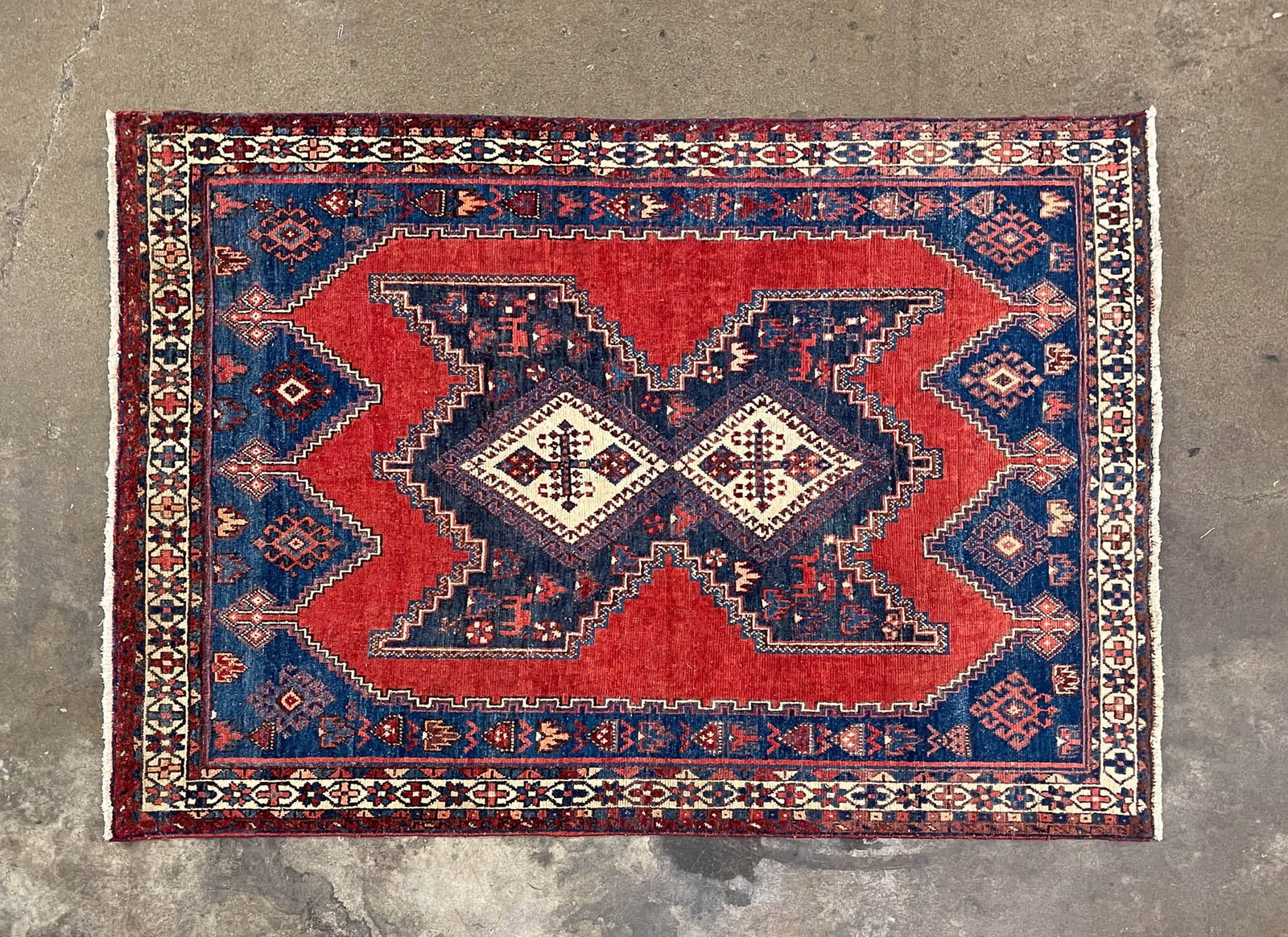 SIROAN WOOL AREA RUG.: Persia, 20th Century. Wool. Red field, blue and cream medallion, cream and red borders and geometric and stylized pattern. 4' 11"w. 7' 11"l.