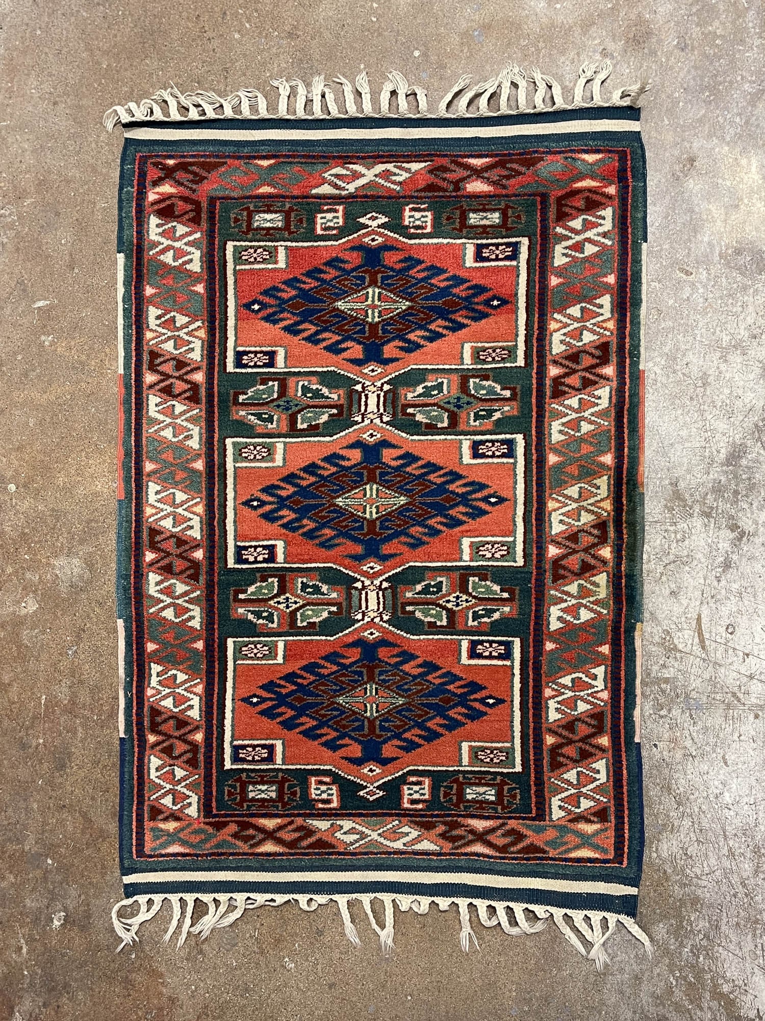 CAUCASIAN WOOL AREA RUG.: Middle East, 20th Century. Wool. Three rectangular medallions in rust red with dark blue, brown and cream diamonds surrounded by green field, rust blue and green borders and multicolored geometric pat