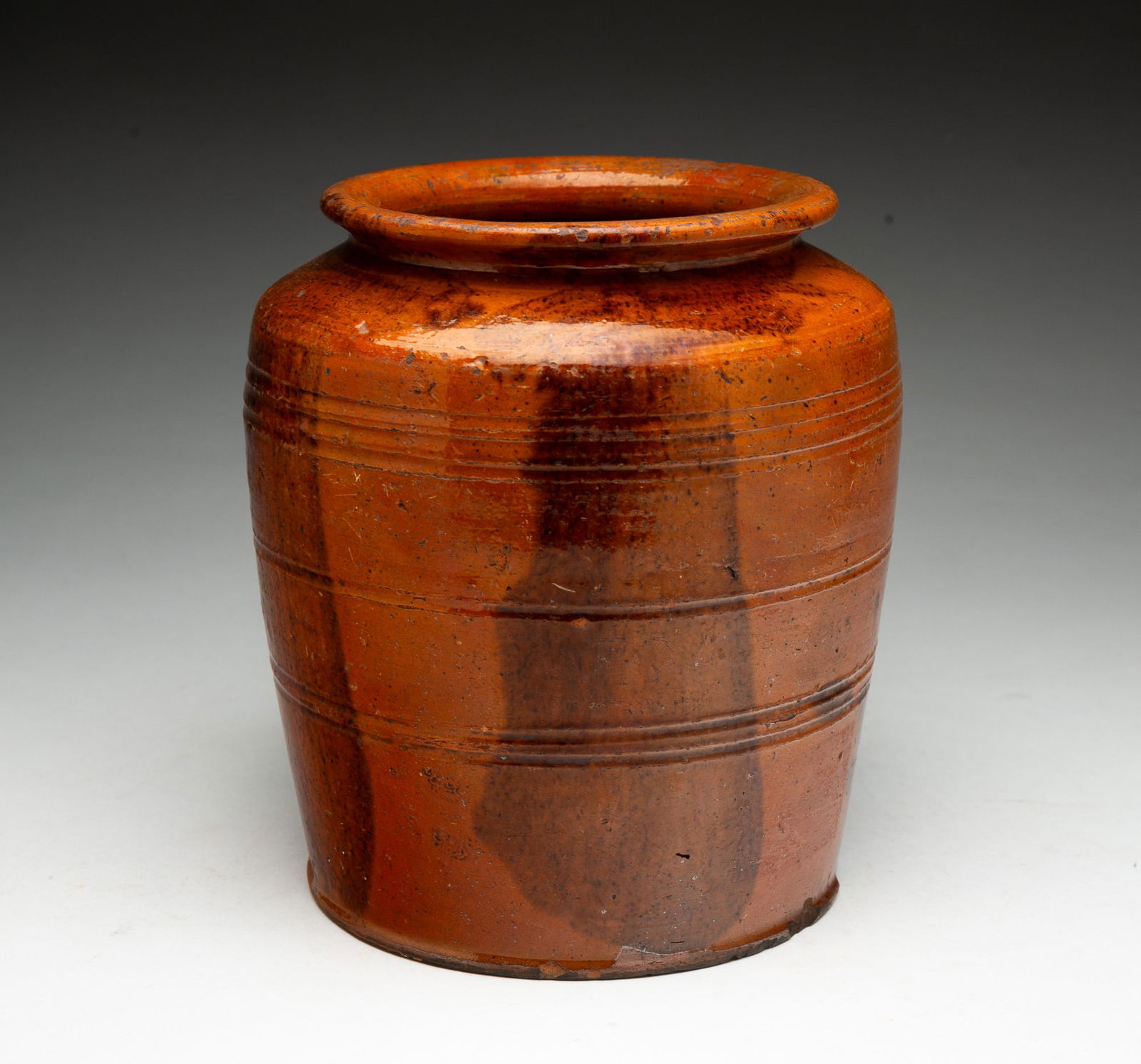 AMERICAN GLAZED AND TOOLED REDWARE JAR.: American, 19th Century. Jar with high orange and brown glaze, incised bands, and flared lip. 7.25"h.