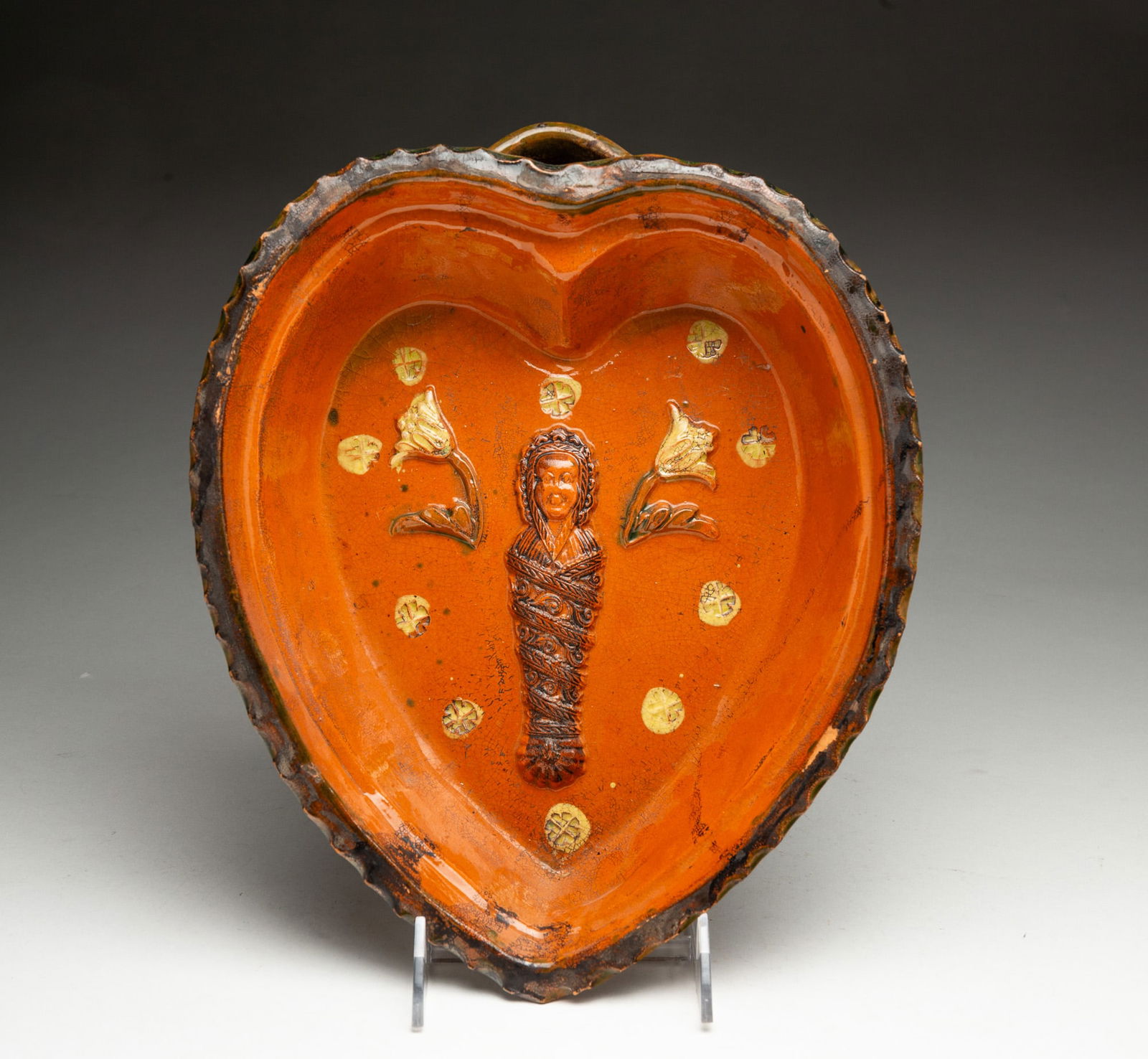 REDWARE HEART FORM FOOD MOLD.: European, 19th Century. Crimped top edge and an interior decoration of an applied woman wrapped in cloths, flowers, and impressed rosettes. 2.75"h. 9.5"w. 11.75"d.