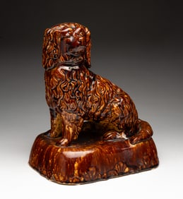 AMERICAN YELLOWWARE SEATED SPANIEL WITH ROCKINGHAM GLAZE.