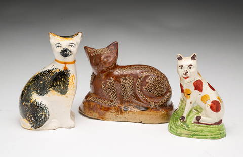 THREE ENGLISH CAT FIGURINES.: English, 19th Century. A Wheldon spotted cat on a green base. 3.25"h., a Staffordshire cat with tan and black sponged decoration 3.75"h., and a buff clay with brown glaze and coggled decoration reclin