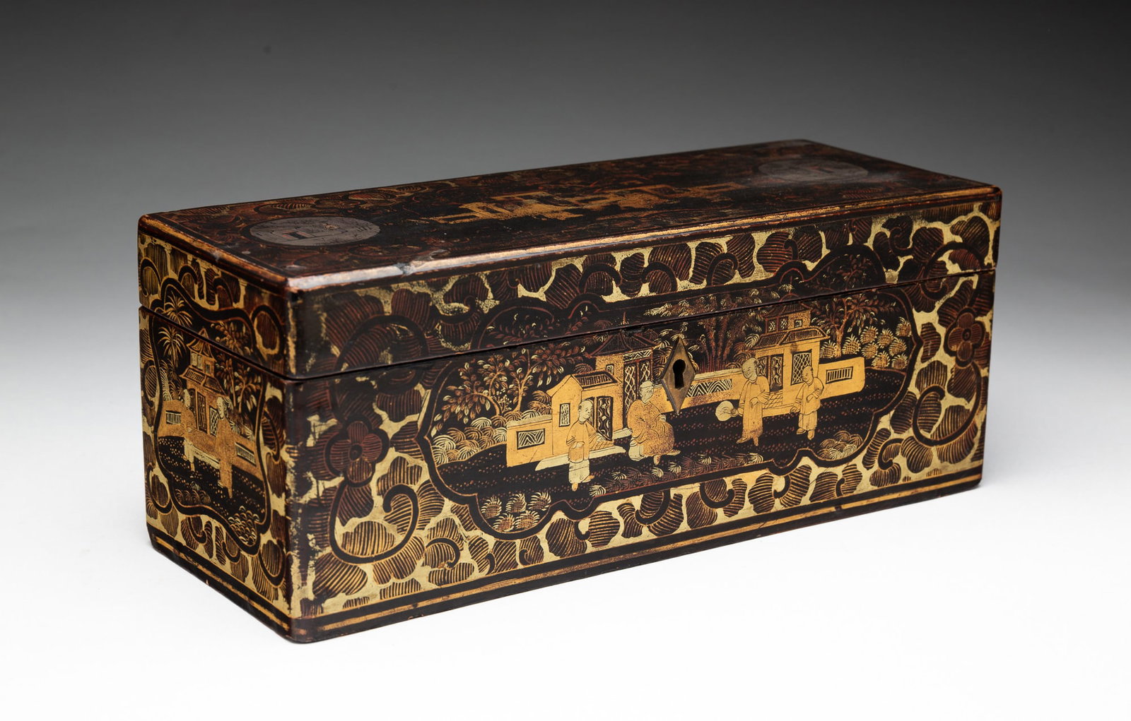 CHINESE EXPORT BLACK AND GILT-LACQUERED GLOVE BOX.: Chinese, Mid-19th Century. Chinoiserie decorated with figures in front of buildings and trees surrounded by scrolling flowers, the hinged lid opening to an interior fitted with a lacquer tray. 4"h. 10