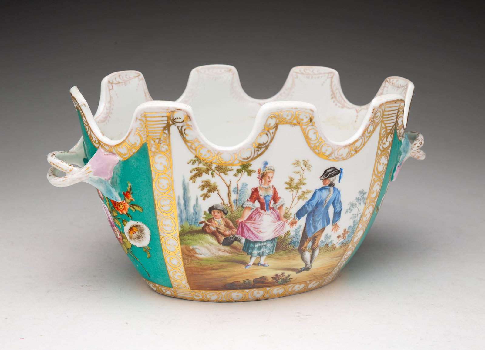 DRESDEN POLYCHROME AND GILT PORCELAIN MONTEITH.: Germany, 19th Century. Oval form with crenellated top rim and two entwined handles, painted with panels of scenes of figures playing music and dancing between panels of flowers on green ground, with g