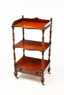 EARLY VICTORIAN MAHOGANY THREE-TIER WHATNOT.: English, ca.1860. Mahogany. Boldly turned corner posts with finials, shaped gallery edge on top, three shelves with serpentine front edges over a single dovetailed drawer, short turned legs with brass