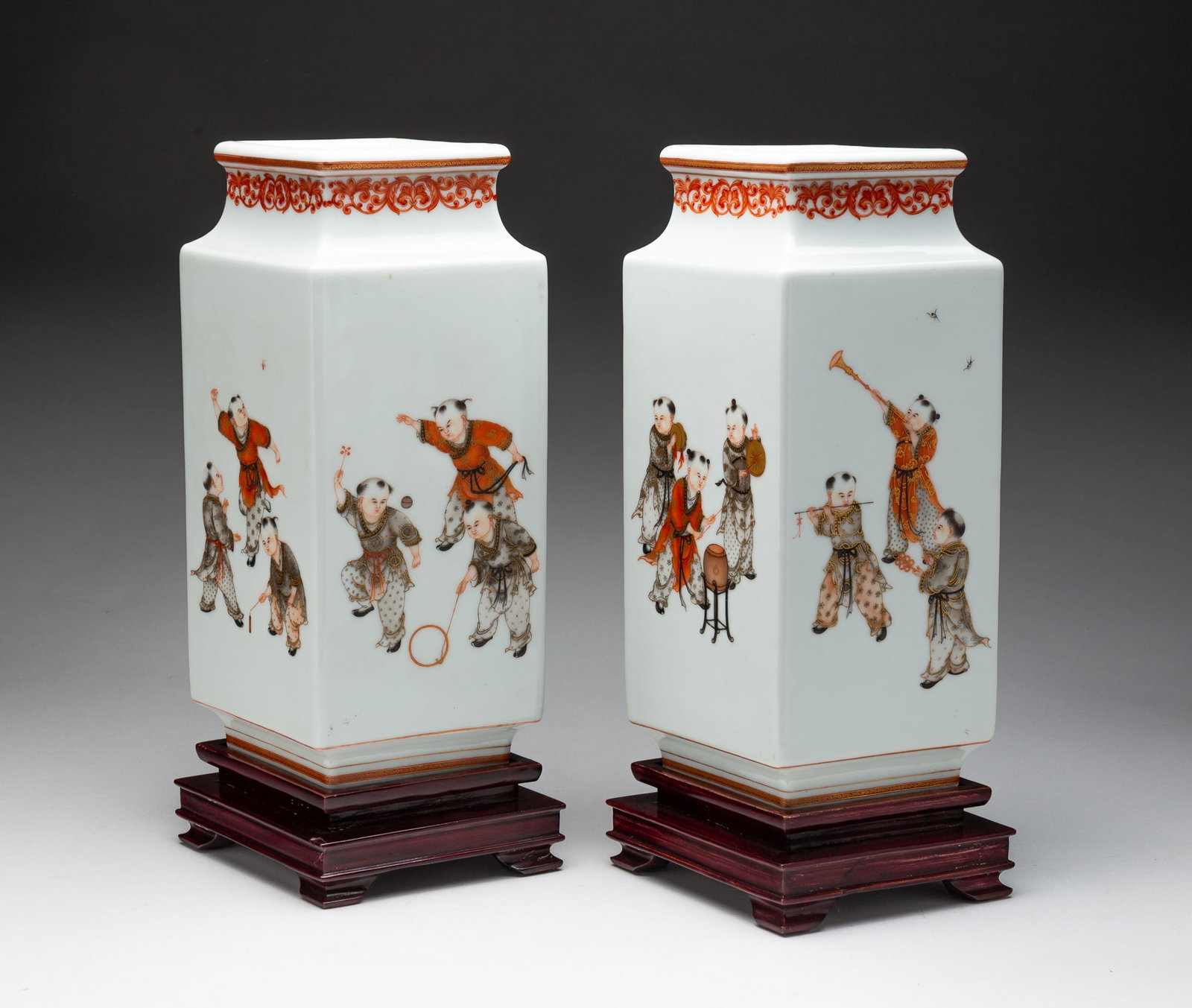 PAIR OF CHINESE FAMILLE ROSE DIAMOND FORM PORCELAIN VASES.: China, late 19th Century. The neck decorated with a scrolling foliage motif, the sides decorated with scenes of children playing, raised on diamond form stepped wooden bases, unmarked. Each (with base