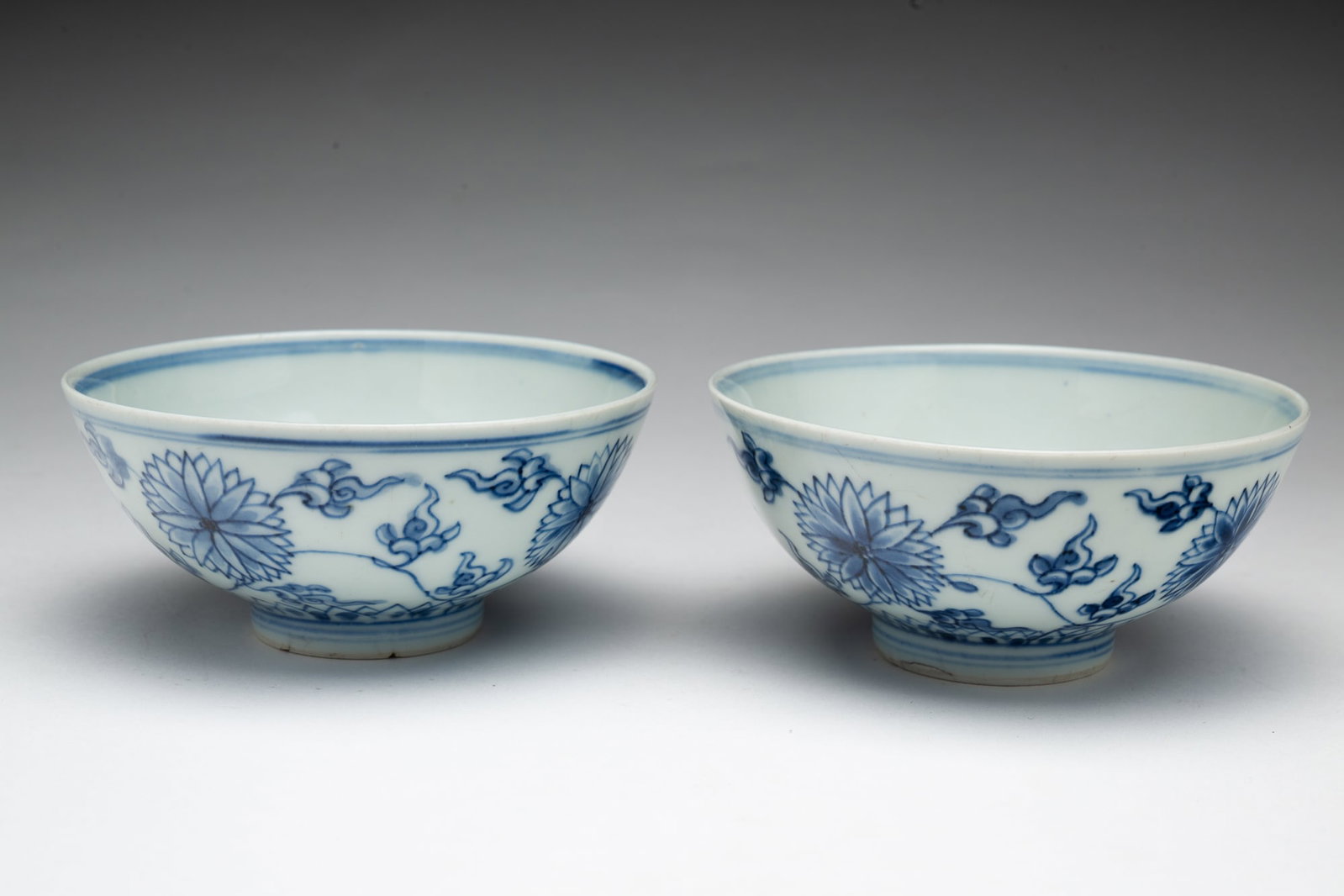 TWO CHINESE BLUE AND WHITE PORCELAIN BOWLS.: China, 19th Century. The interior decorated with blue bands and a flower, the exterior with chrysanthemums, clouds, and lotus leaves, each with a Yongzheng mark on underside, each in a blue gift box. 
