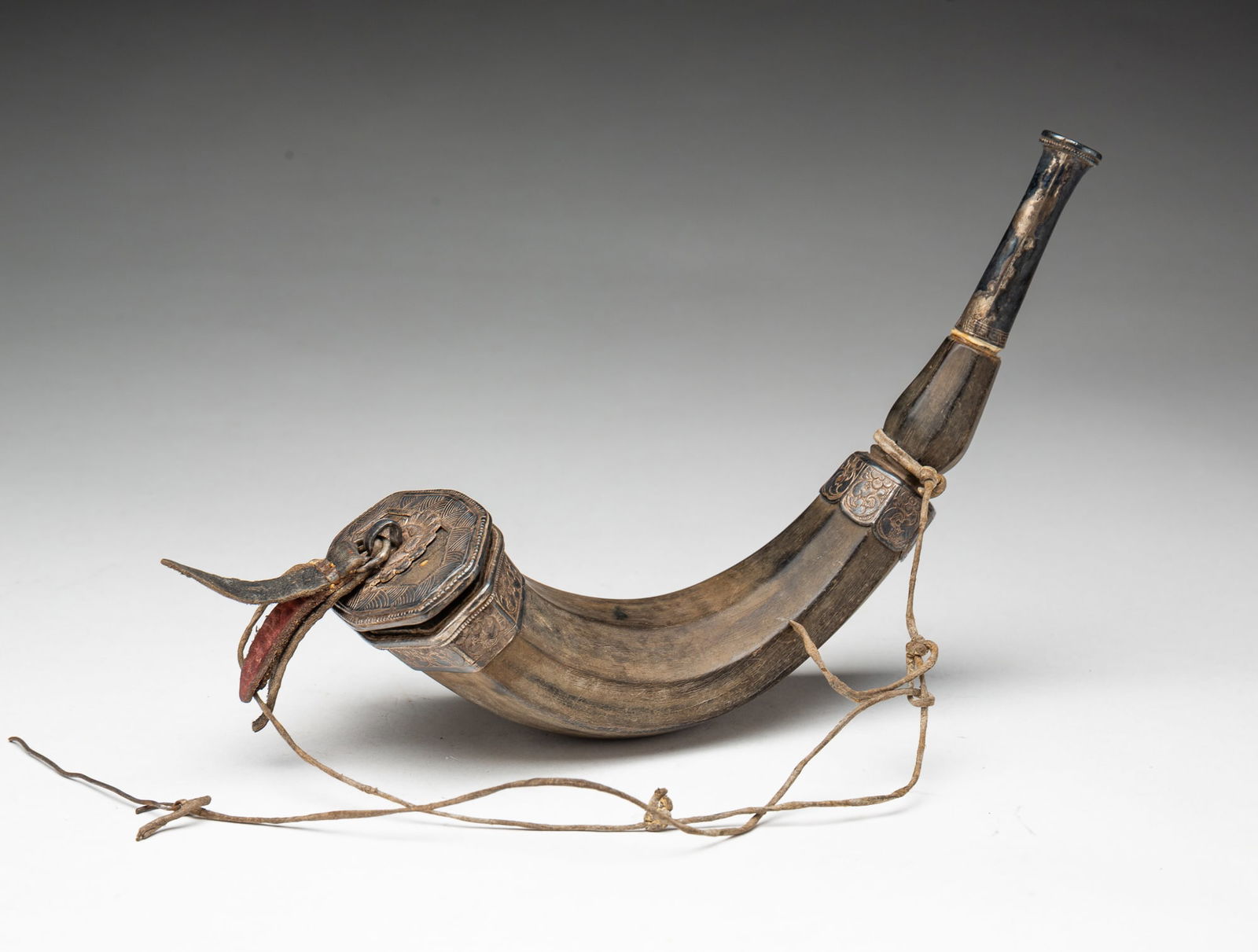 SILVER MOUNTED AND CARVED HORN POWDER FLASK.: European, 19th Century. Curving horn carved in facets with silver mountings incised with floral and geometric motifs, and having a leather tassel on the plug. 9"l.