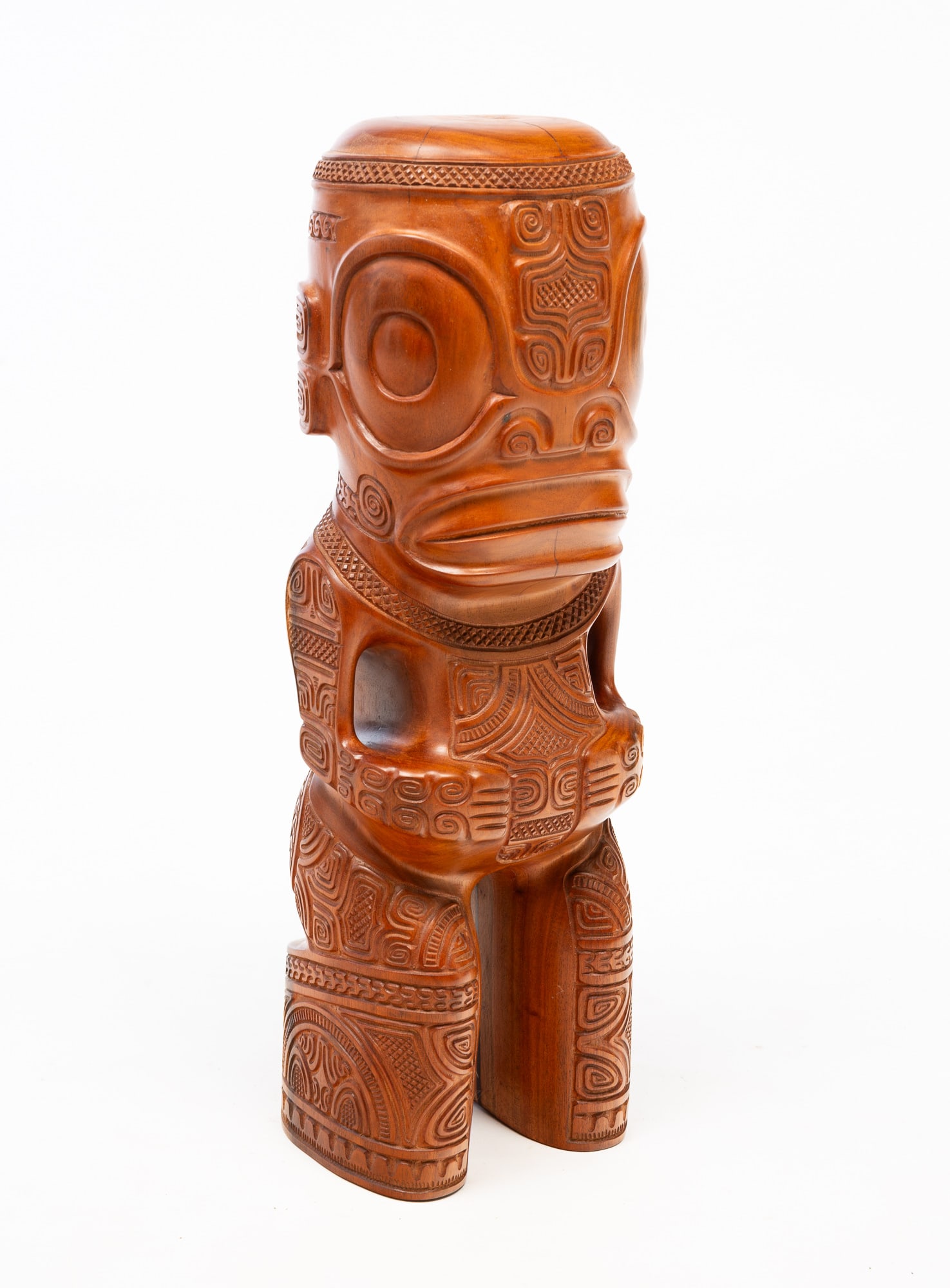 SIGNED FRENCH POLYNESIAN CARVED WOOD TIKI FIGURE.: Taihoe, Nuku-Hiva Island, 20th Century. Elaborately carved figure having large eyes and a large mouth, with hands on belly, carved all over with swirls and geometric motifs, the underside of one leg s