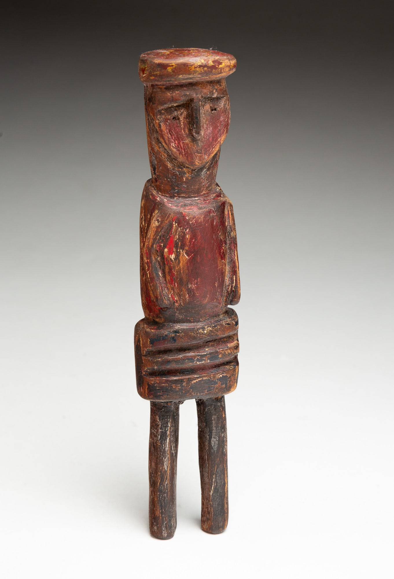 PRIMITIVE CARVED AND PAINTED WOODEN FIGURE.: American, 19th Century. Simple carved figure with flat hair, simple facial features, and two stick legs, and nice paint history. 8.5"h.