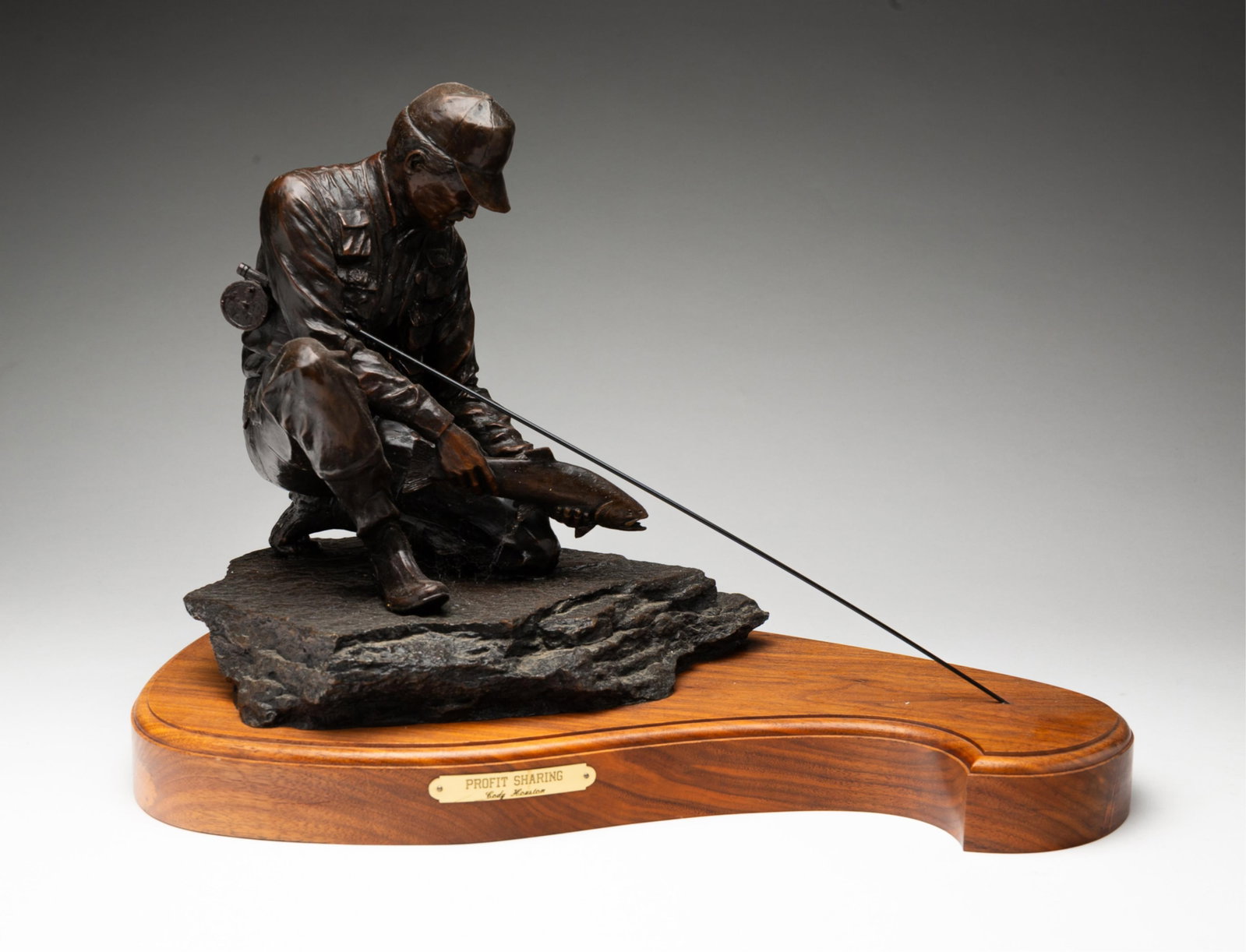 CODY HOUSTON (AMERICAN, B. 1941) "PROFIT SHARING" BRONZE SCULPTURE.: American, 1996. Depicting a kneeling fisherman holding a fish and a fishing rod, edition 10/45. Signed, dated, and editioned on base, the sculpture mounted on a shaped wooden base with brass plaque. O