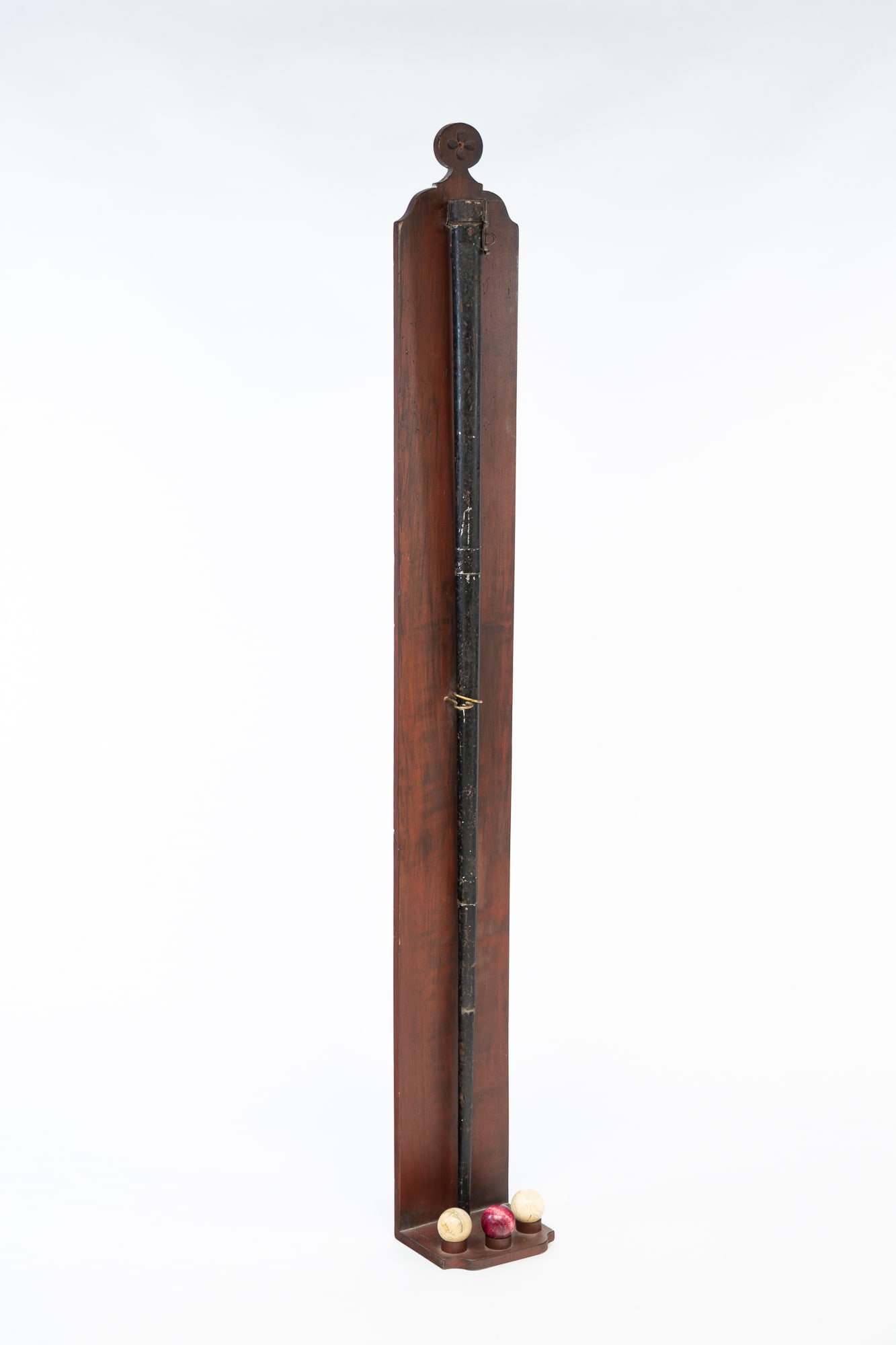 PAINTED TIN BILLIARD CUE CASE, BONE BILLIARD CUE, AND THREE BILLIARD BALLS ON CUSTOM WOOD STAND.: American, 19th Century. Black painted tin case with hinged lid containing a bone cue on a custom red-washed pine stand with carved round finial top and shaped crest, with three balls of natural materi
